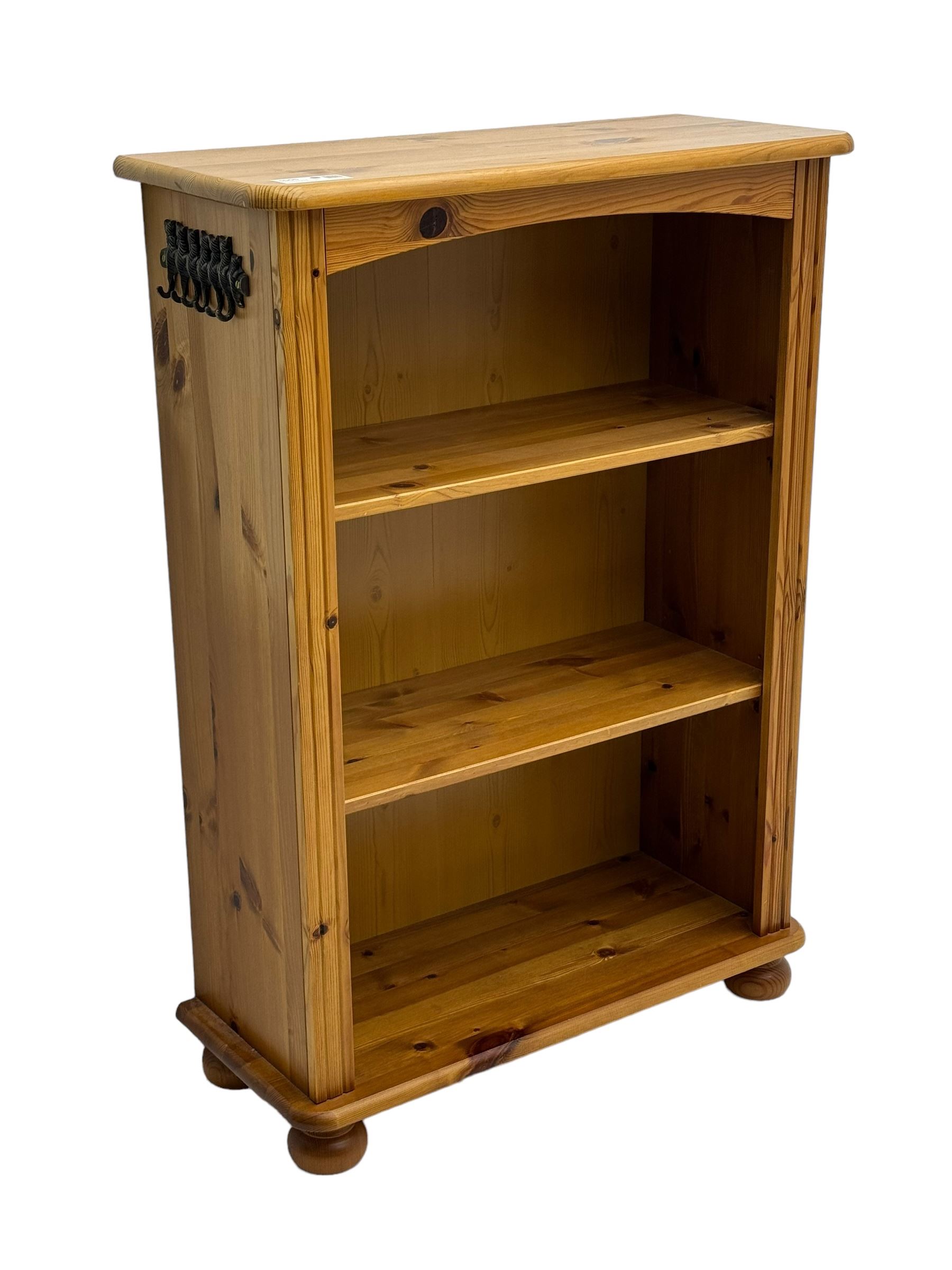 Traditional pine open bookcase, featuring arched top section flanked by fluted side supports, two adjustable shelves and cast iron coat hook with cat motif to the left side, standing on round bun feet 