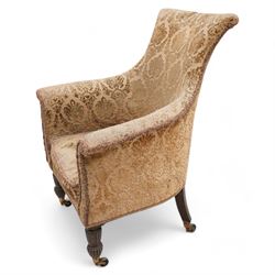 Early 19th century mahogany framed armchair, curved form with rolled cresting, upholstered in raised foliate pattern fabric, tub seat with shaped and rolled arms, on turned and reed carved front feet, brass cups and castors 