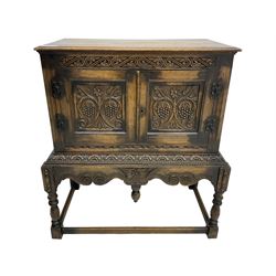 Jacobean Revival carved oak cupboard, moulded rectangular top over S-scroll carved frieze and two doors, the panelled doors carved with stylised plant motifs, on stand decorated with lunettes and shaped apron with hanging turned pendant, on turned supports united by stretchers 