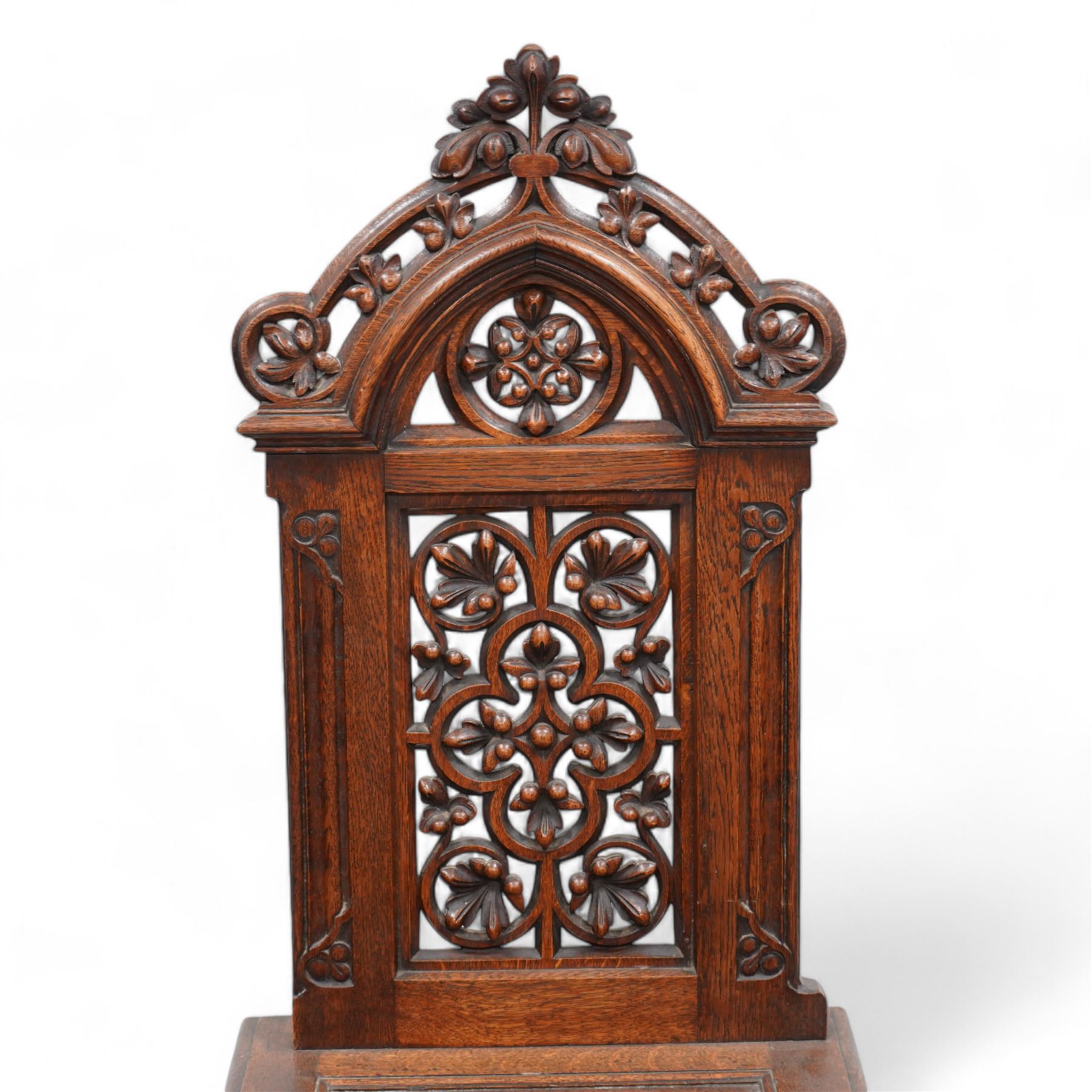 In the manner of Augustus Pugin - 19th century Gothic Revival oak hall chair, shaped pediment carved and pierced with foliate decoration, panelled back pierced with floral quatrefoil and scrolled decoration, panelled seat with moulded seat frame with projecting curved corners, on moulded X-framed supports united by turned and faceted stretcher, on sledge feet 