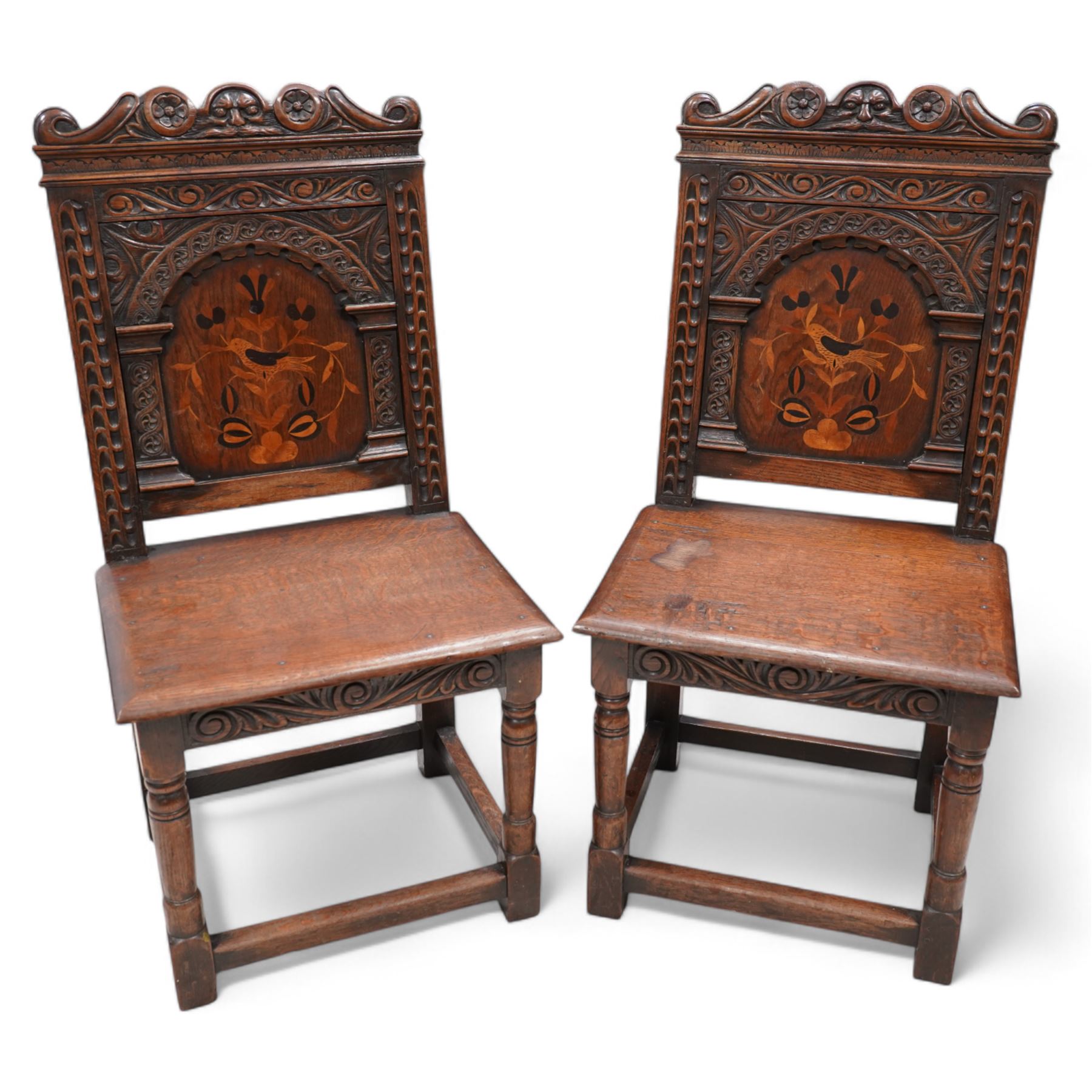 Pair of 19th century Dutch style marquetry oak hall chairs, cresting rail carved with a central green man mask with flanking scrolls, the panelled back inlaid with a bird motif within a guilloche carved arch, panelled seat over scrolling foliate carved apron, on ring turned supports united by box stretcher