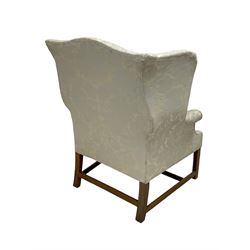 Georgian mahogany framed wingback armchair, upholstered in floral pattern silk damask fabric, wide seat enclosed by rolled arms, on chamfered square supports united by plain stretchers 