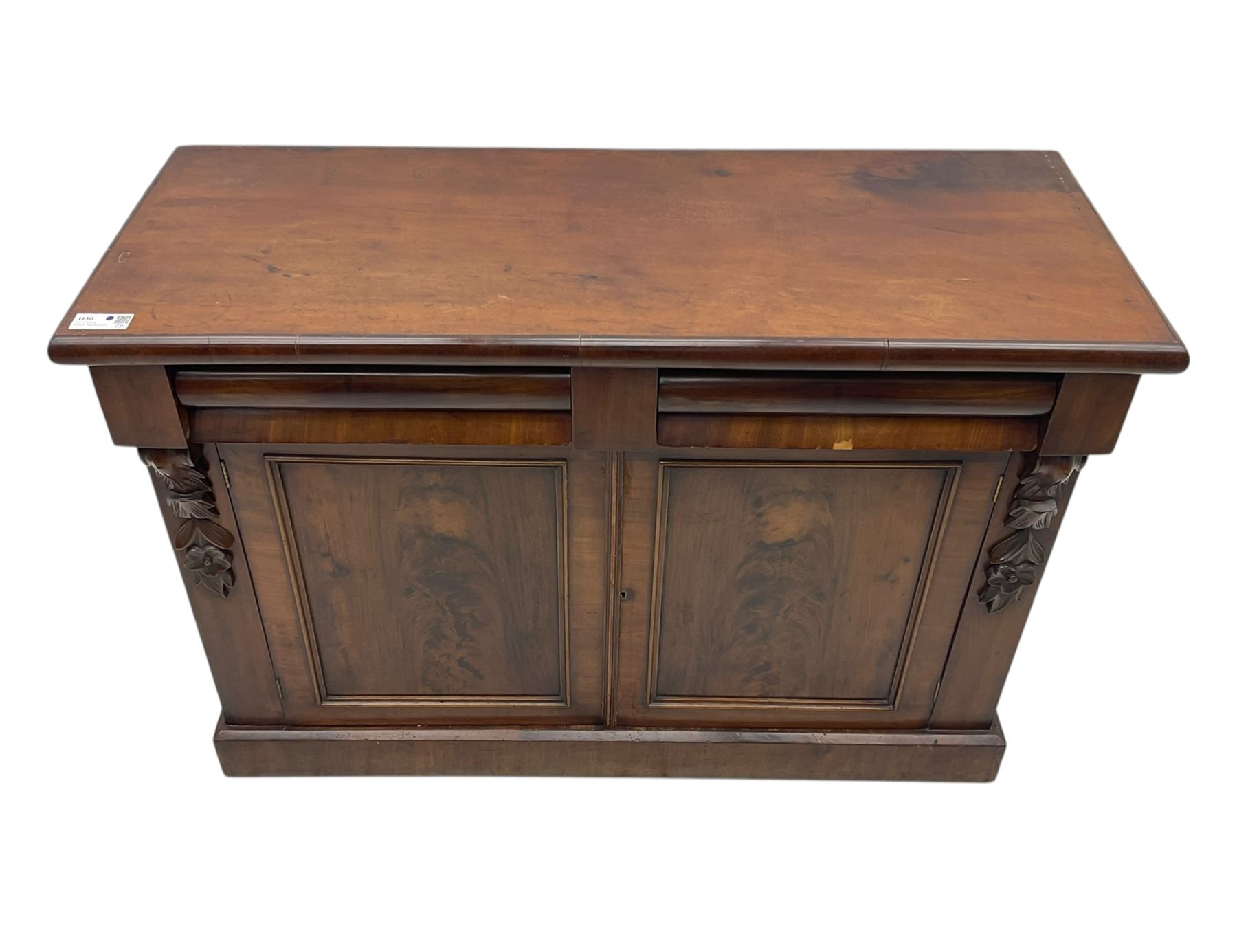 Mid 19th century mahogany sideboard, rectangular top over two frieze drawers with rounded edges, flanked by floral carved corbels, over two panelled cupboard doors, raised on a plinth base