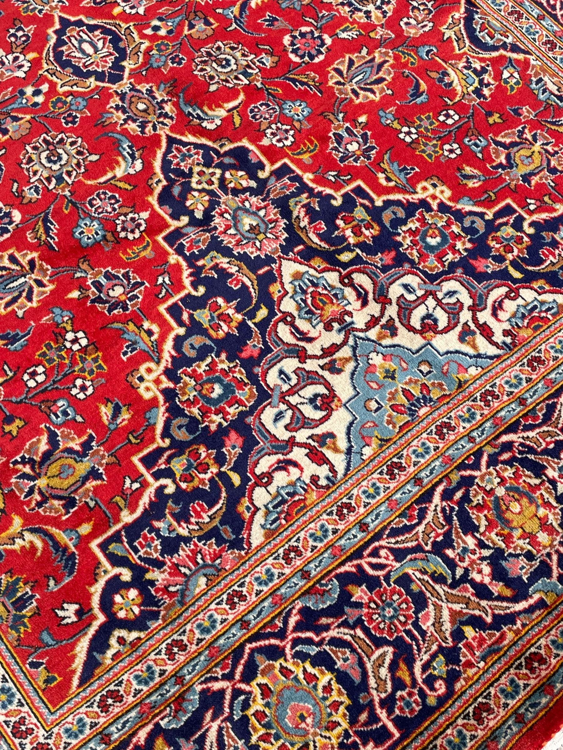 Persian Kashan crimson ground rug, overall arabesque design, the field decorated with swirled leafy branches and palmettes, indigo ground border decorated with repeating pattern, within guard stripes 