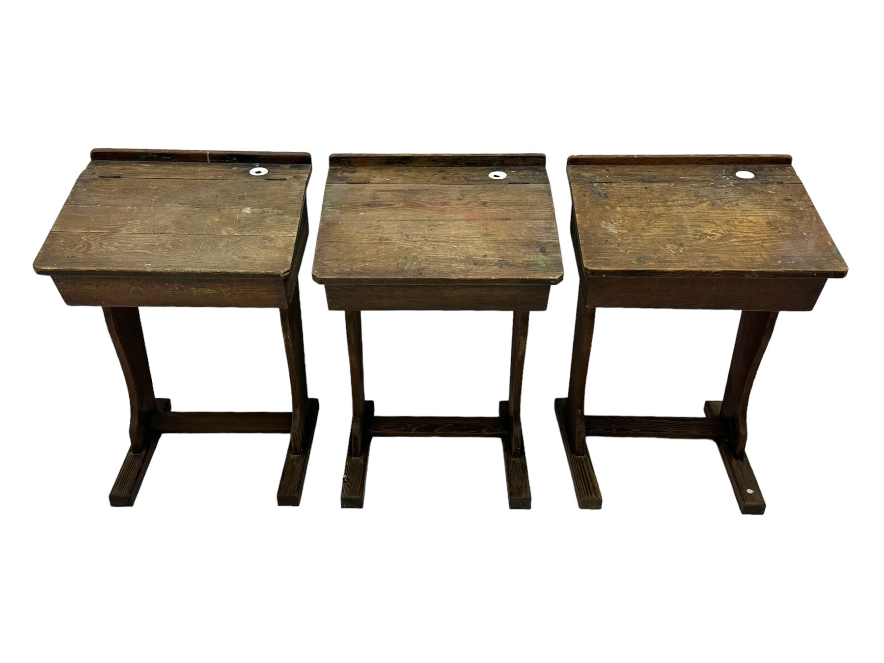 Three pitch pine school desks, each with rectangular lift-top with recessed ink well enclosing storage compartment, on trestle supports joined by stretcher