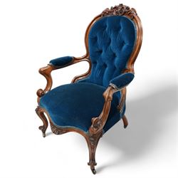 Victorian walnut framed open armchair, curled leaf carved cresting rail over scrolled and shaped arms, upholstered in buttoned blue velvet fabric, on cabriole feet