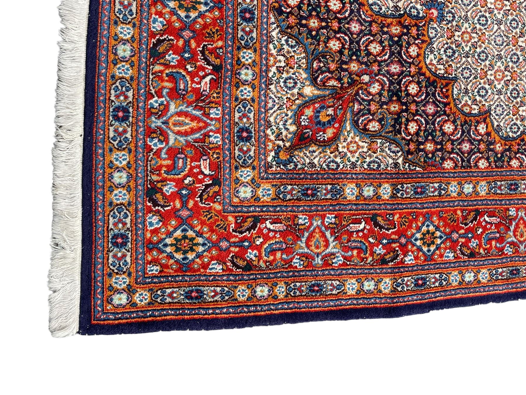 Persian Bidjar ivory and indigo ground rug, large central rosette medallion surrounded by floral herati motifs, crimson ground border decorated with repeating palmettes, within guard stripes decorated with small flower head motifs 