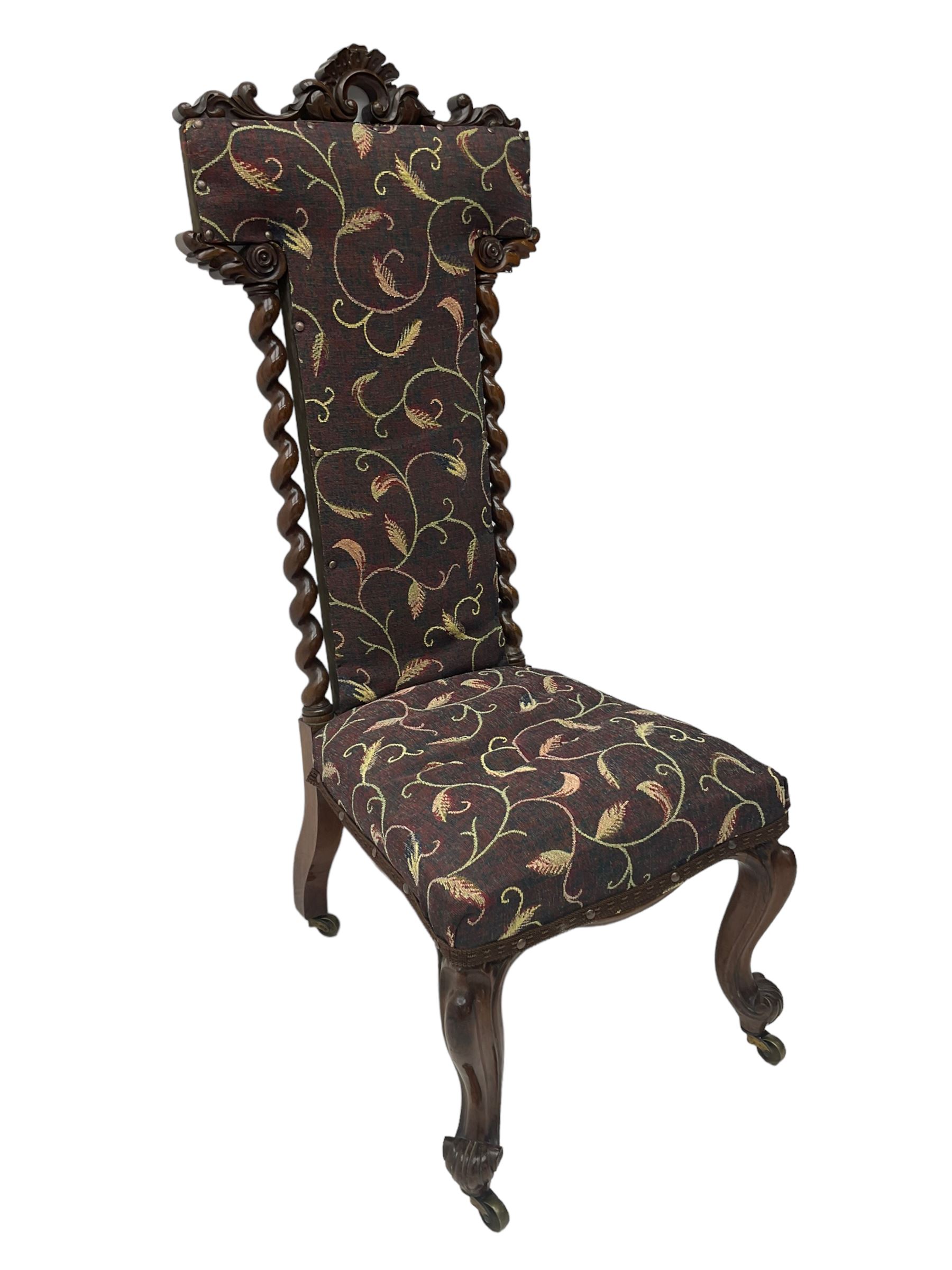 Victorian walnut prie-dieu chair, cresting rail carved with cartouche and extending scrolling foliage, back flanked by spiral turned column uprights, upholstered in foliate patterned fabric, raised on cabriole supports with scroll feet and castors