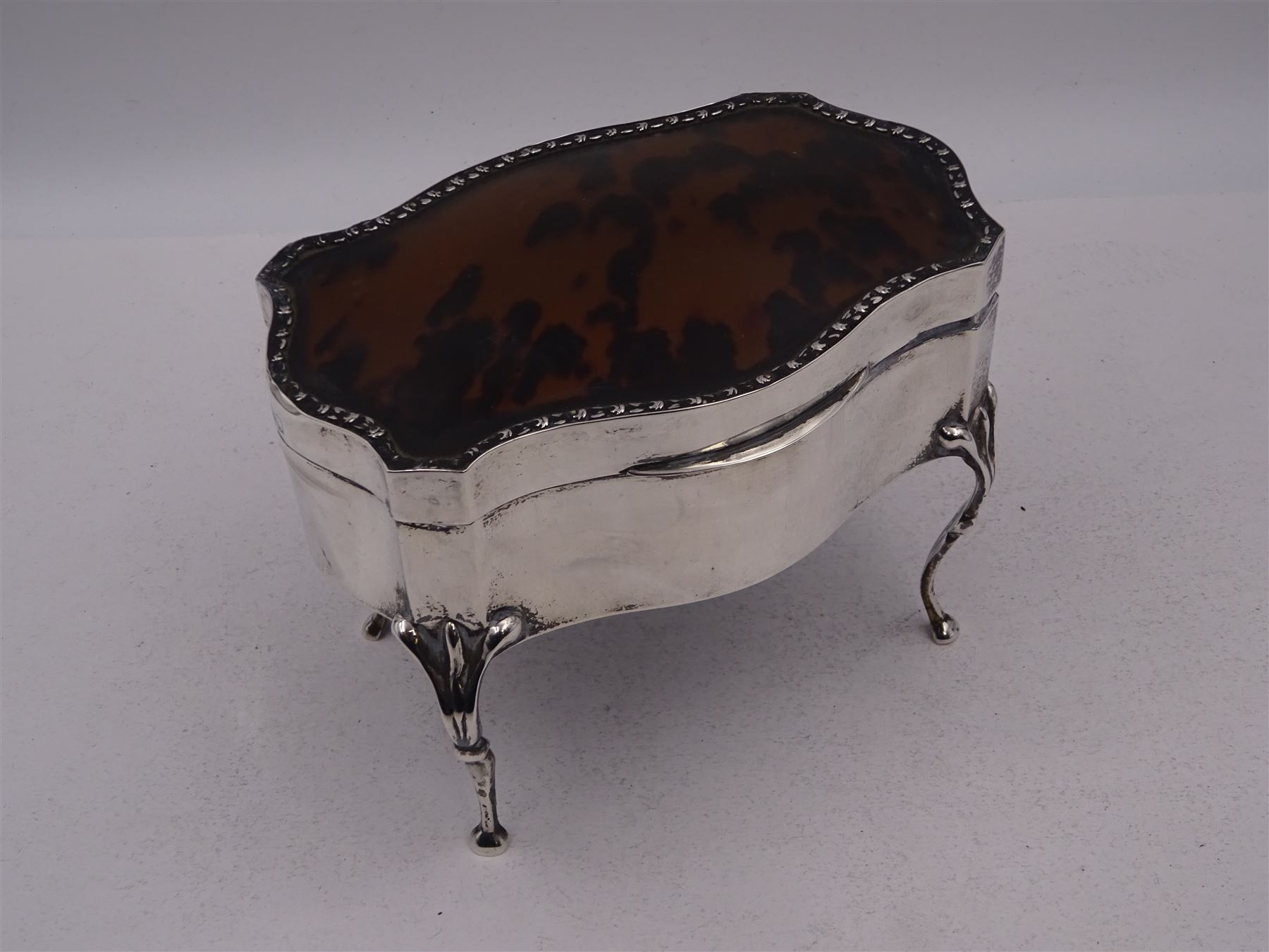 Early 20th century silver mounted jewellery casket, the slightly domed hinged cover set with a tortoiseshell panel, with a embossed floral border, opening to reveal a pleated silk lined interior, upon four cabriole legs, hallmarked Charles Boyton & Son Ltd, London 1913, H10cm