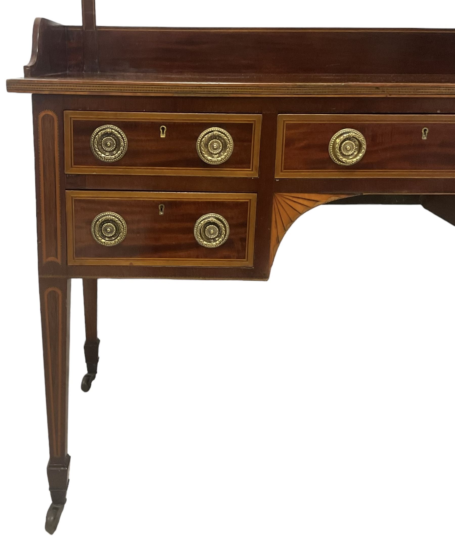 Edwardian inlaid mahogany kneehole dressing table, raised shaped oval bevelled mirror back, fitted with five drawers with banding and stringing, on square tapering supports with castors