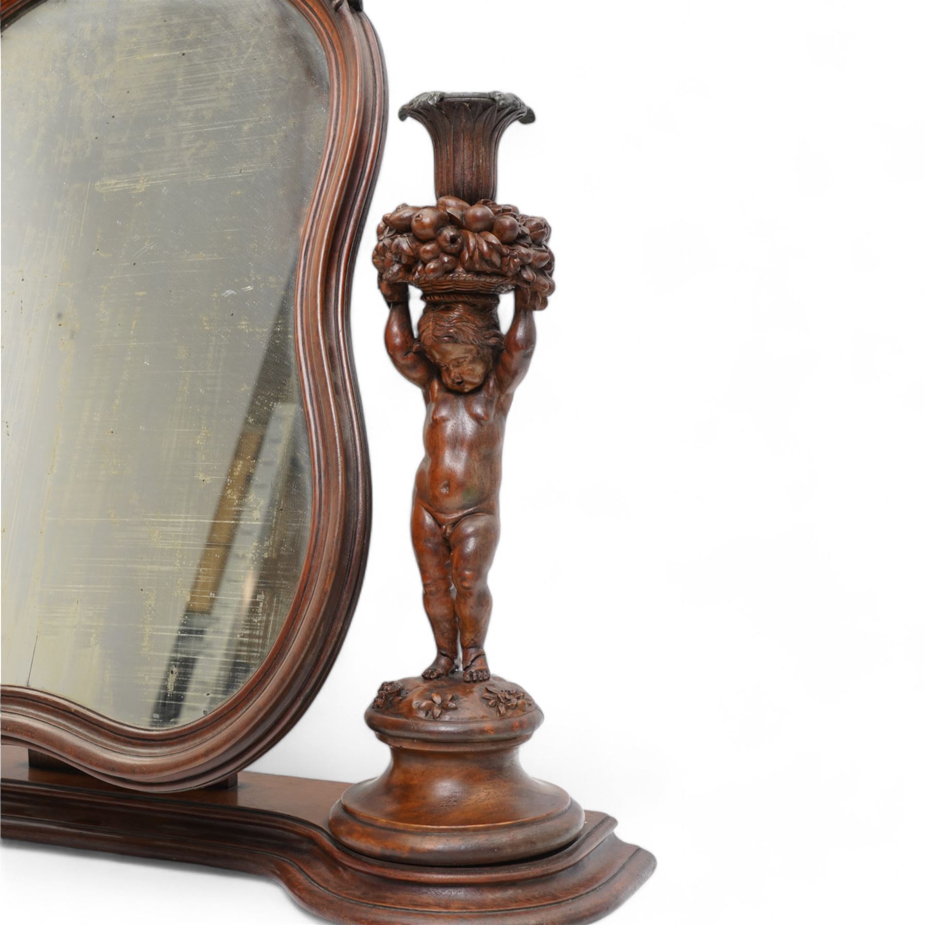 Late 19th century Northern European carved walnut dressing table mirror, the moulded arch top frame carved with flower heads and foliage, flanked by two putto holding baskets of flowers and fruit with candle sconces, on shaped moulded base, plain mirror plate 