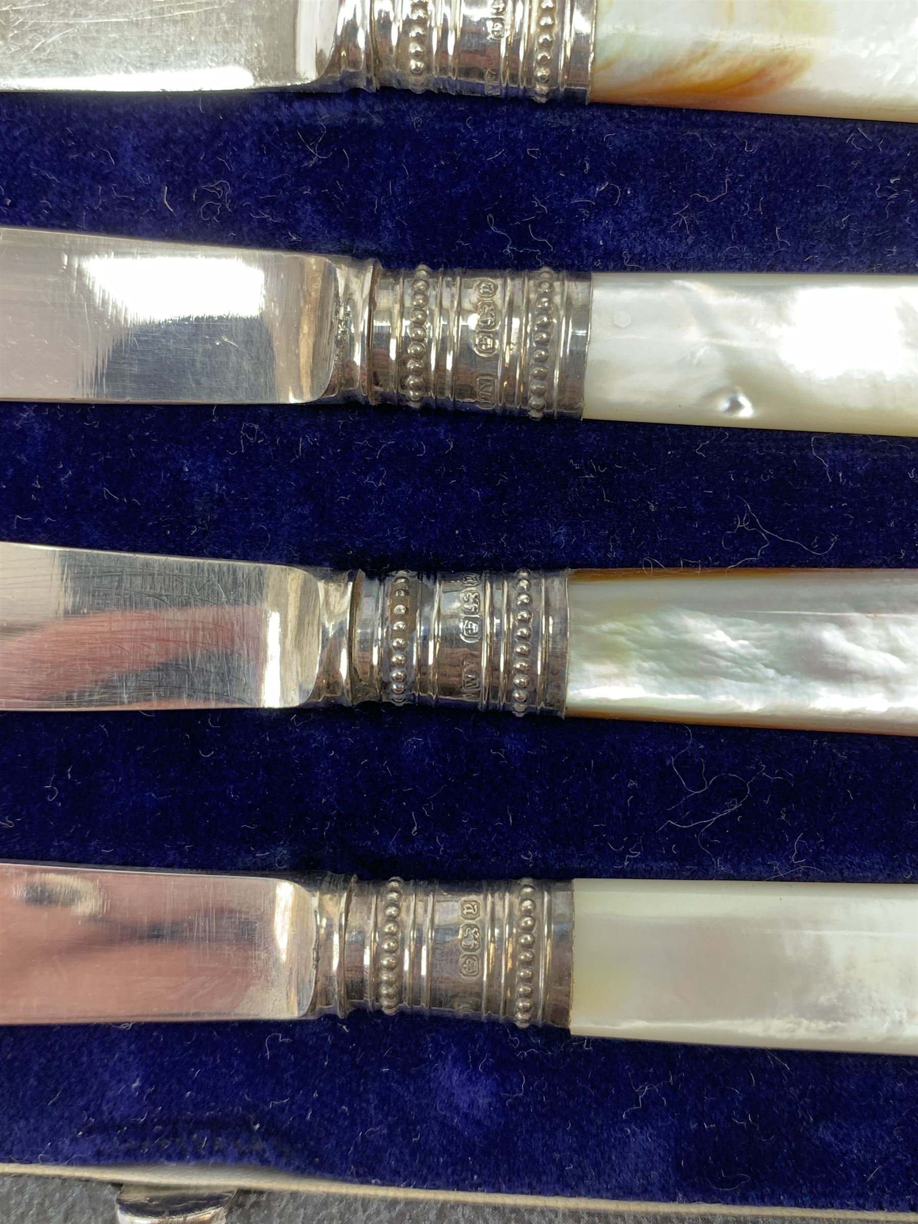 A pair of silver mounted clothes brushes, each with engine turned detail and monogramed central panel, and silver comb mount, all hallmarked Adie Brothers Ltd, Birmingham, date letters worn and indistinct, together with a cased set of six mother of pearl knives with silver ferrules, hallmarked William Yates Ltd, Sheffield 1916, a silver plated bottle coaster, with pierced sleeve and twin handles, marked beneath for Daniel and Arter, Birmingham, and a set of six silver plated coffee bean spoons. 