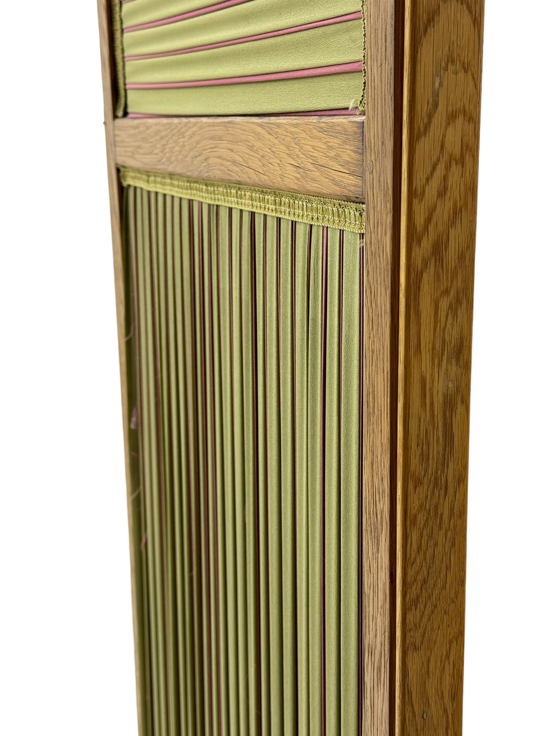 Edwardian oak and fabric folding screen, featuring three panels with oak frames, one side covered in green striped fabric with decorative trim, the reverse side in pink moiré effect fabric, connected by brass hinges