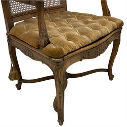 Late 19th century French carved beech open elbow chair, shaped cresting rail carved with central shell and curl leafage, cane work seat and back with buttoned loose seat cushion, the open arms carved with scrolled terminals and acanthus leaves, on cabriole supports with carved decorated united by shaped and moulded x-framed stretchers 