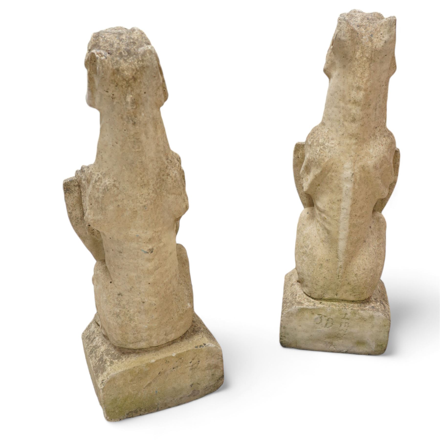 Near pair of cast stone garden seated dragons, snarling jaw holding shield on chamfered base 