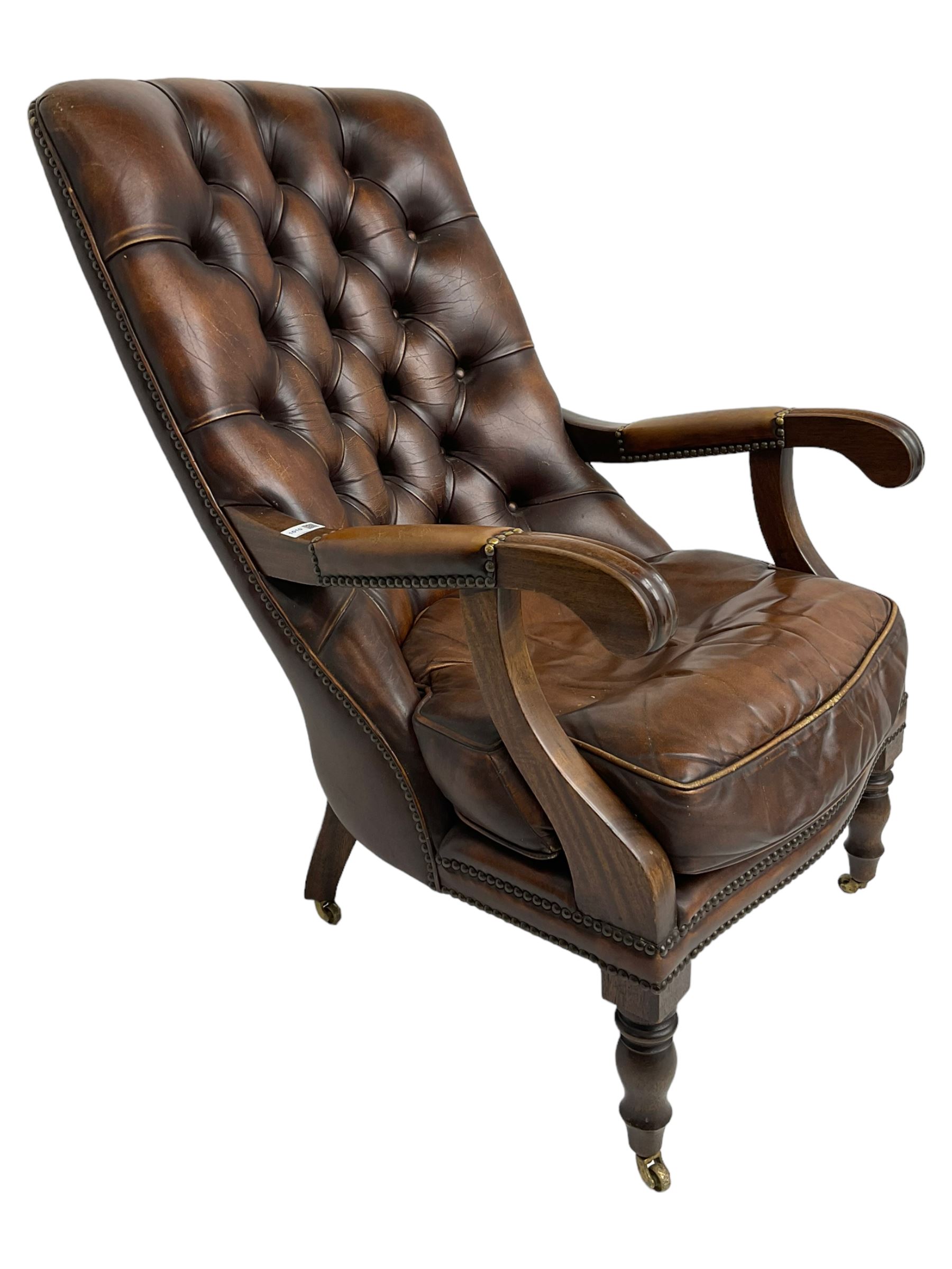 Georgian design mahogany framed library armchair, upholstered in buttoned chocolate brown leather with studwork and loose seat cushion, raised on turned supports with brass castors