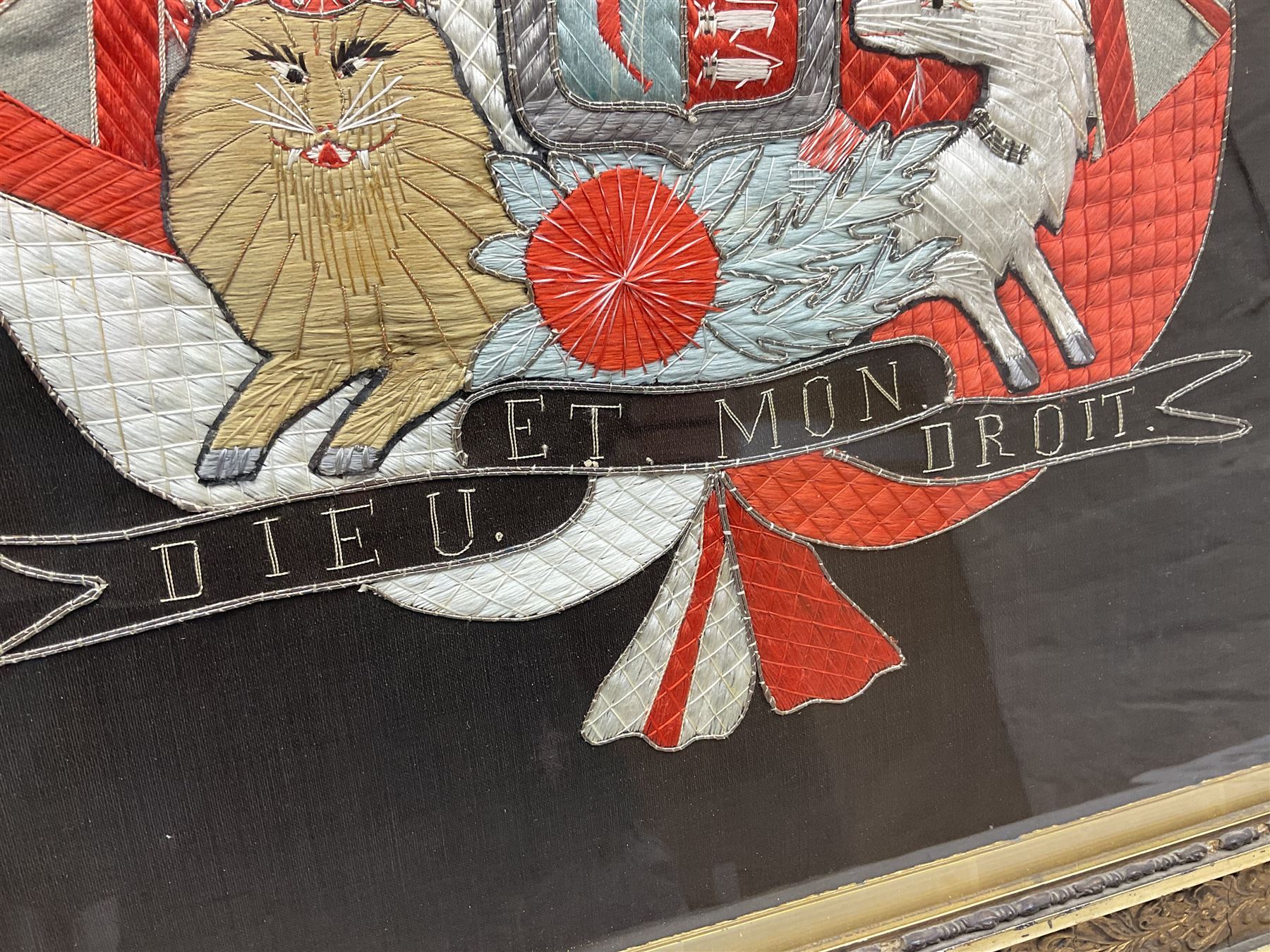 Early 20th century silk needlework panel, depicting a ship in full sail and Royal Coat of Arms to centre, with red and white ensigns to either side, lion and unicorn below with quote 'Dieu Et Mon Droit', upon a black silk ground within gilt frame, H59cm