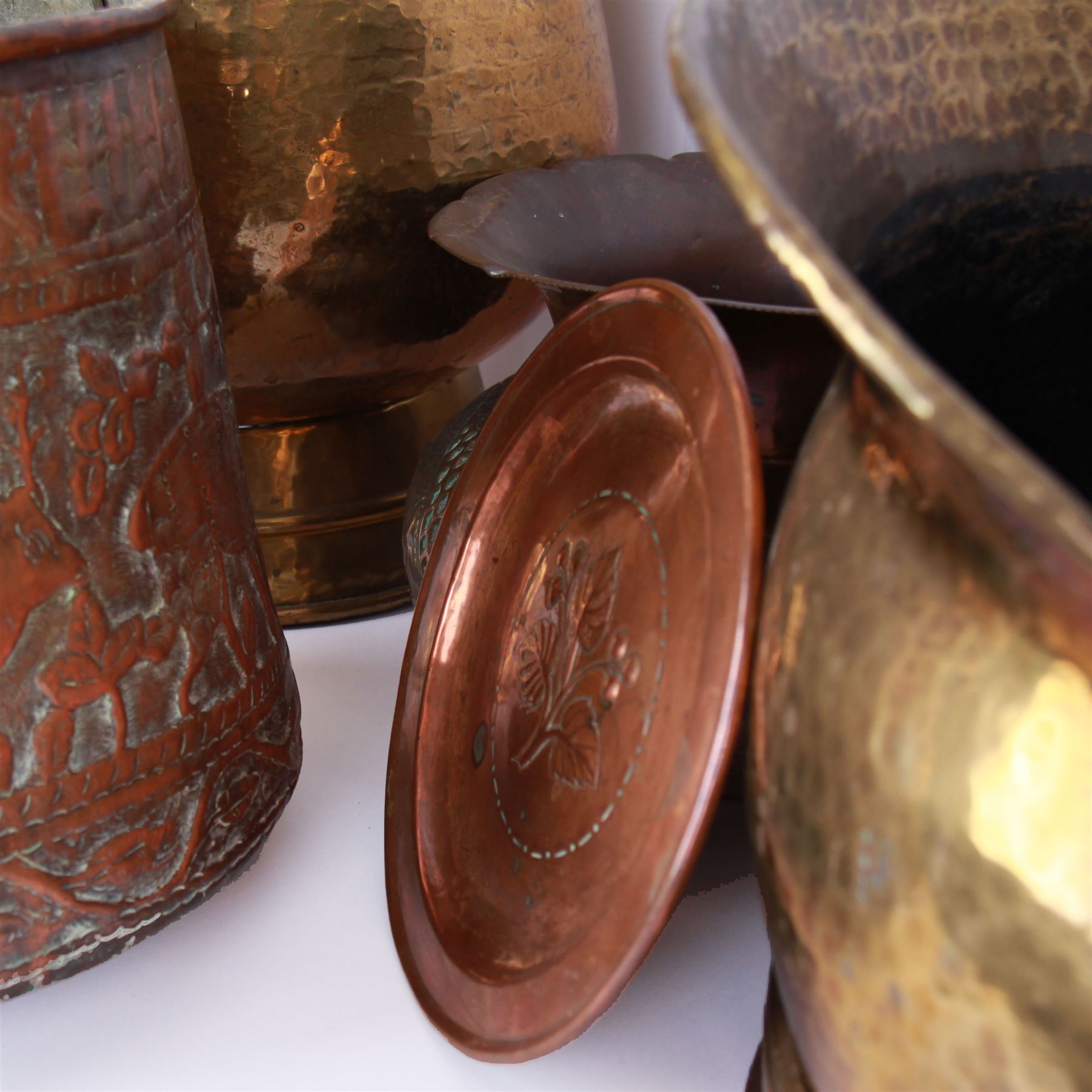 Middle eastern copper bucket, with chased and embossed band of animal decoration, together with a copper jardinière embossed with floral panels, copper plate with embossed leaf motif and two brass helmet shaped coal scuttles, bucket H26cm