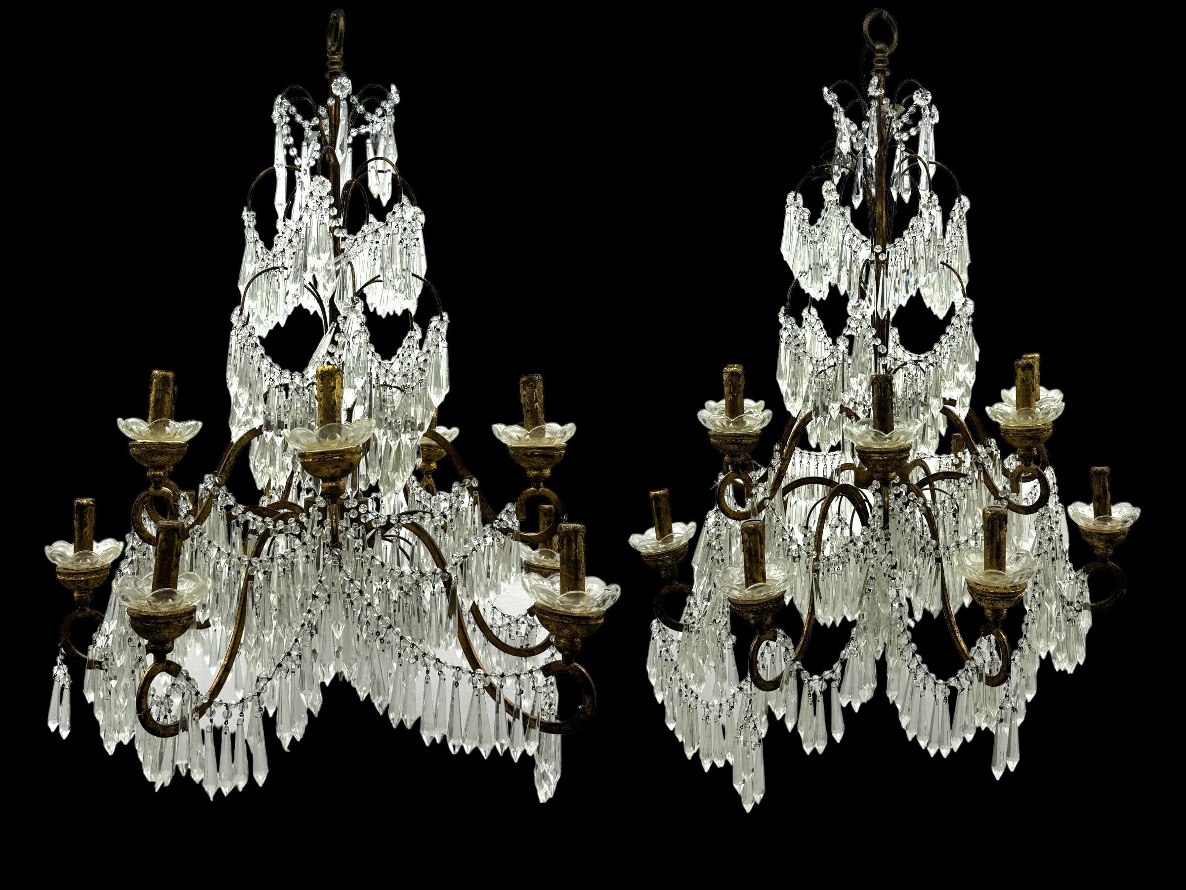 India Jane Interiors - pair of contemporary gilt bronze and crystal chandeliers, the framework featuring scrolling arms and garlands of crystal beads, each with twelve candle-style light fixtures with scalloped glass bobeches, adorned with multiple tiers of cut glass prisms, terminating in a central finial with a suspension loop