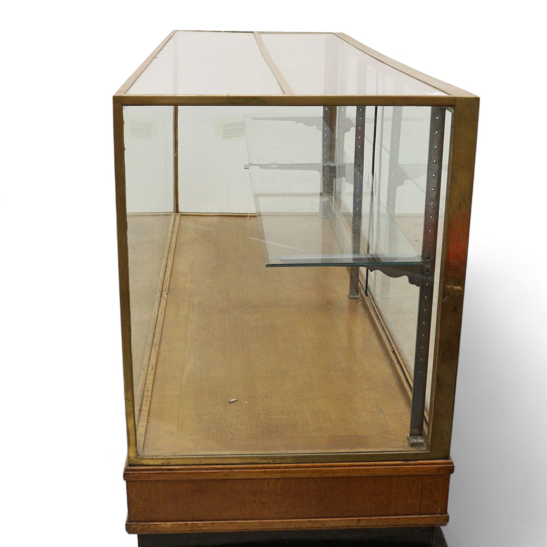 Early 20th century glazed oak and brass bound shop's display cabinet or haberdashery cabinet, fitted with two sliding glass doors, two glass shelves on chromed metal supports, black finish block feet