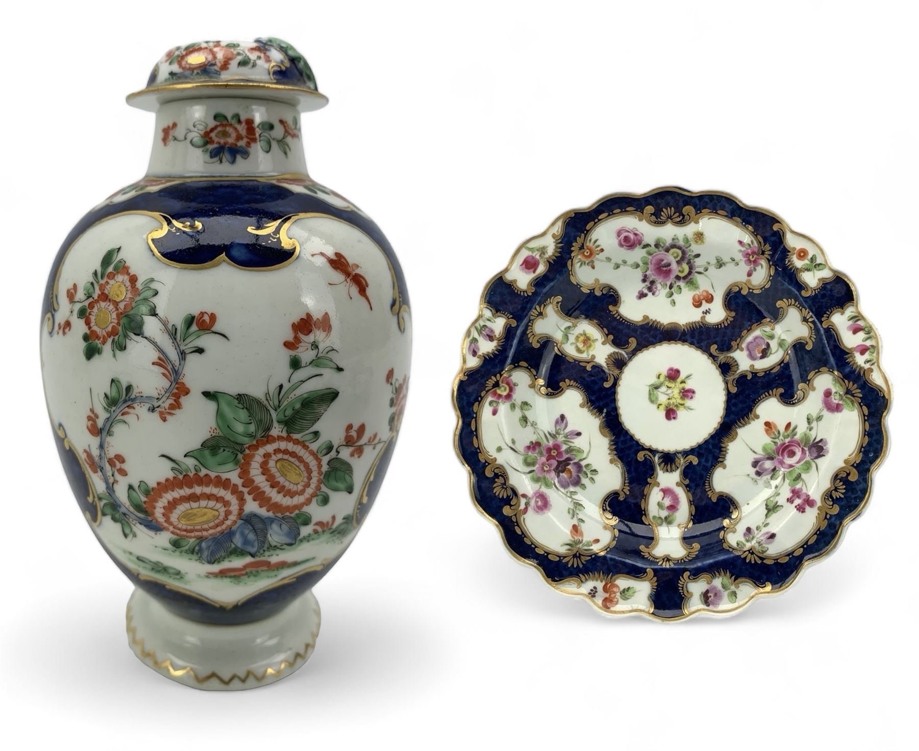 18th century Worcester tea caddy, of oval form and painted in the Kakiemon palette with reserves of flowers against a blue scale ground, H14cm together with a similar Worcester circular dish, painted with floral sprays, within a scalloped edge, blue crescent mark beneath, D19cm (2)