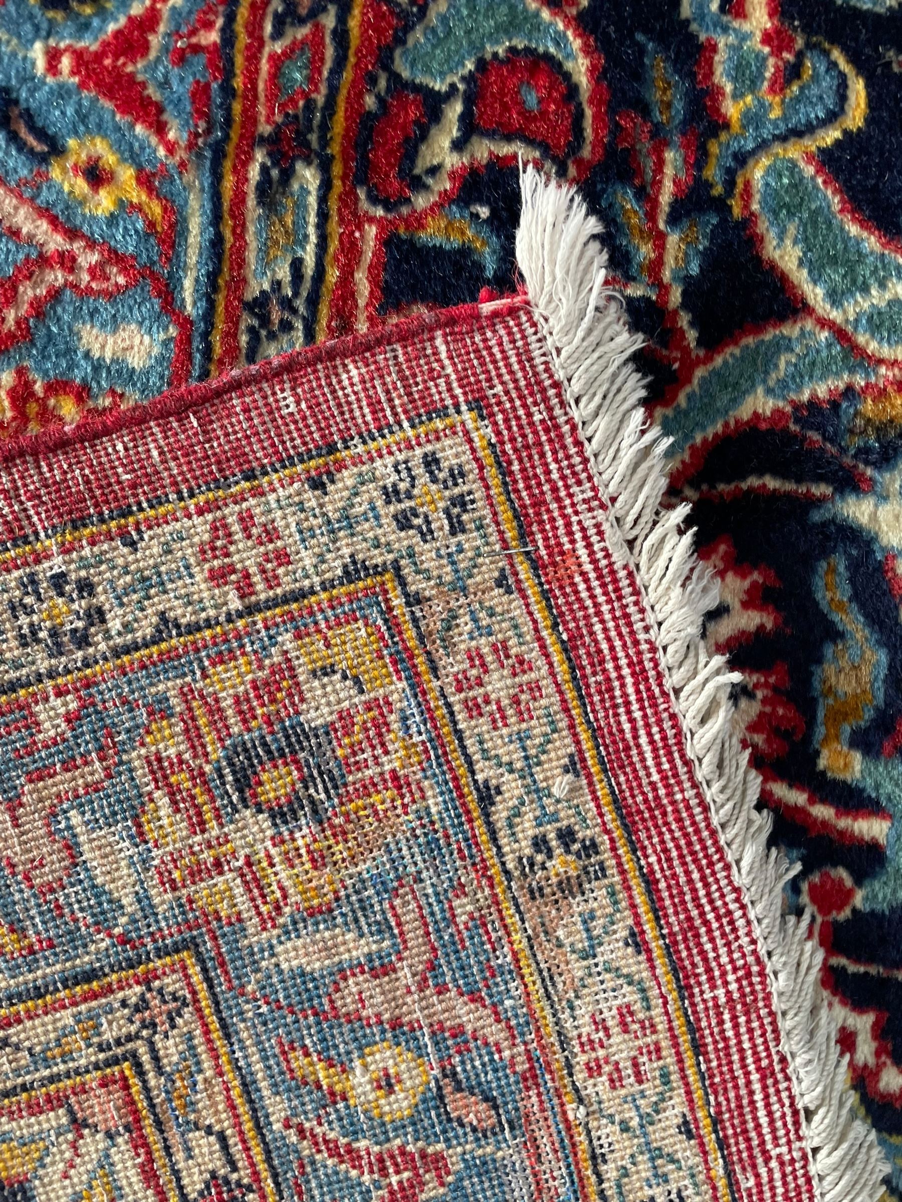 Persian Kashan crimson ground carpet, central rosette medallion on a field of trailing foliate branches decorated with palmettes, scrolling border with repeating plant motifs and flower heads, enclosed within floral pattern guard stripes