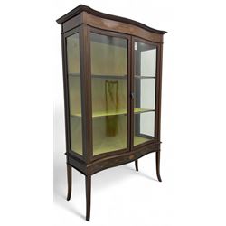 Edwardian inlaid mahogany serpentine display cabinet, projecting moulded cornice over figured frieze inlaid with tailing bellflowers and central fan motif, enclosed by two glazed doors, on square tapering supports with splayed terminals 