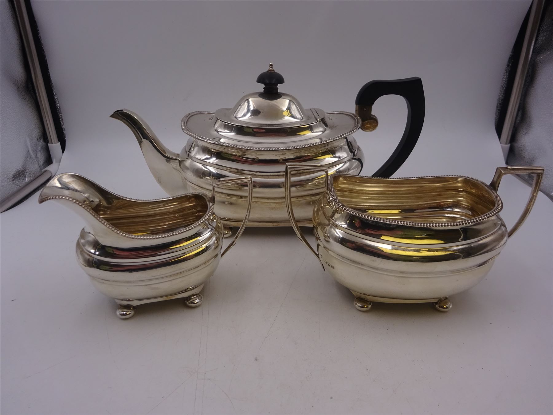 Silver three piece tea service, comprising teapot, twin handled open sucrier and a milk jug, all of oval part fluted form and upon four bun feet, the teapot with black plastic handle and finial, hallmarked S Blanckensee & Son Ltd, Chester 1930, teapot H16cm