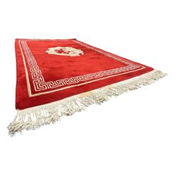 Chinese washed woolen red ground rug, central circular dragon motif in ivory, framed by a decorative Greek key border in matching ivory tones, finished with fringed ends