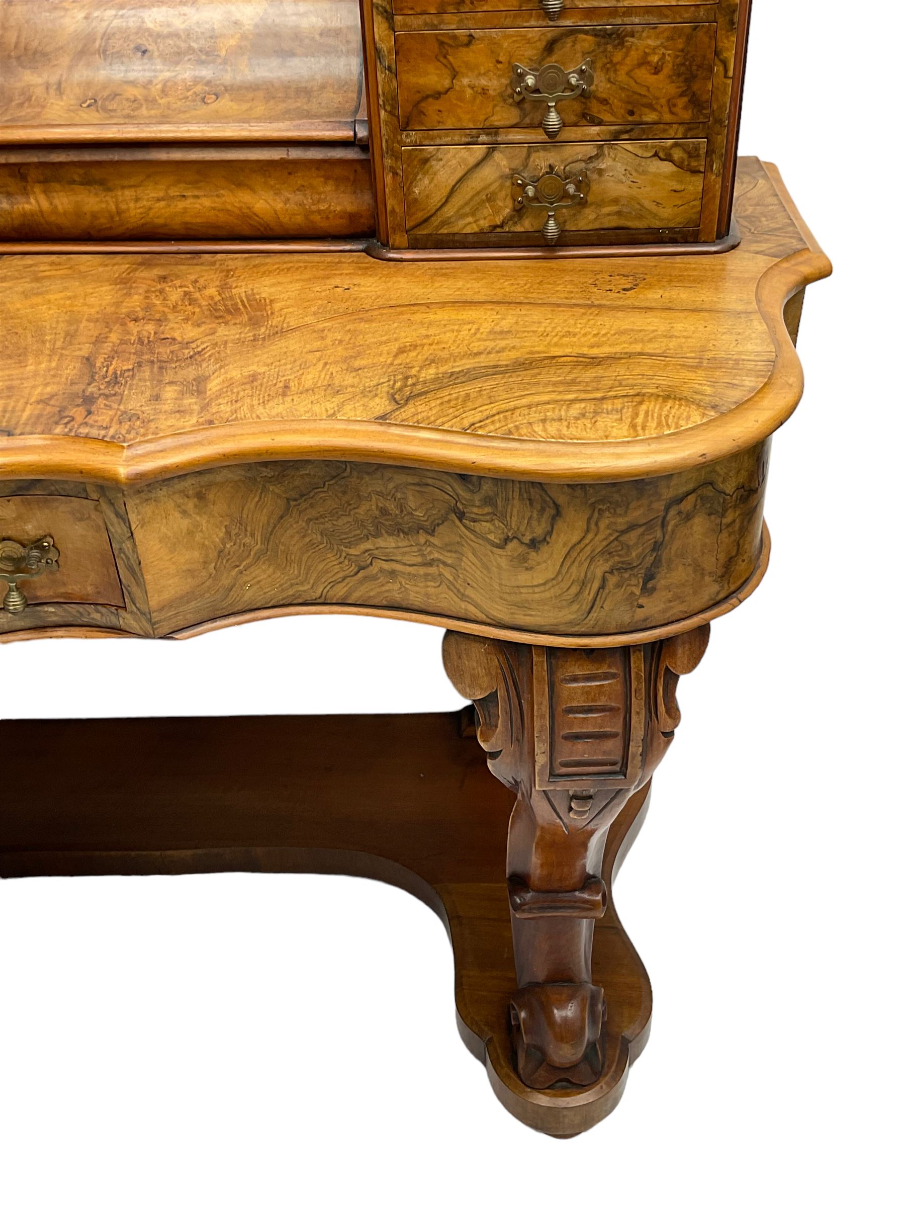 19th century figured walnut dressing table, the raised bevelled mirror back in carved foliage frame with scrolled terminals, fitted with central hinged compartment flanked by small trinket drawers, serpentine moulded top over single frieze drawer, on cabriole supports united by a platform base