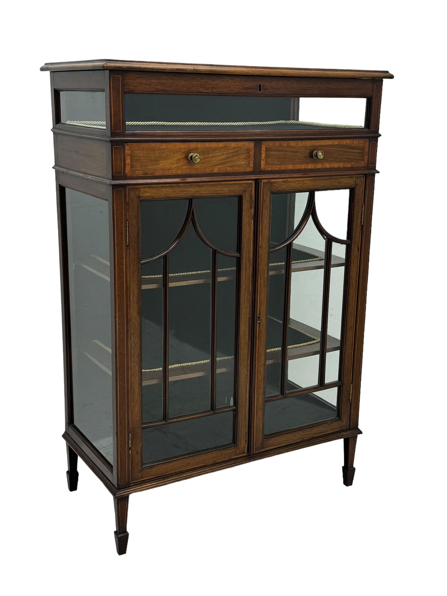 Edwardian mahogany bijouterie display cabinet, featuring satinwood inlay and crossbanding, hinged glazed top fitted with two banded drawers, over two astragal glazed doors enclosing black wool baize lined shelves with gold trim, supported by spade feet