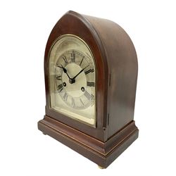 German - 8-day Mahogany mantle clock c1910, in a lancet shaped case on a narrow plinth with brass feet, silvered sheet dial with an engraved chapter ring, Roman numerals and steel spade hands,  with a recoil anchor escapement and rack striking movement sounding the hours and half hours on a coiled gong. With pendulum and key. 