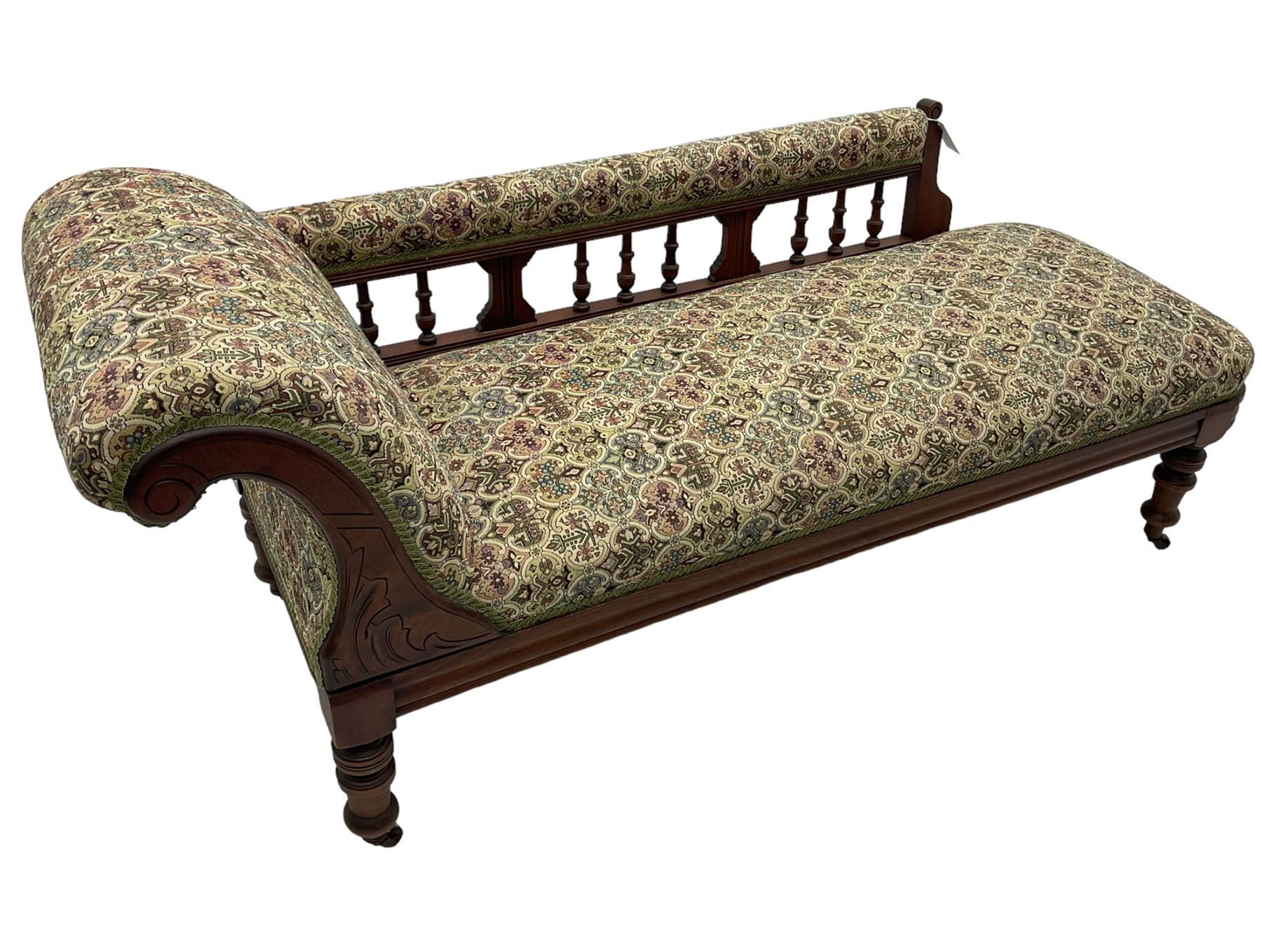 Late 19th century walnut framed chaise longue, upholstered in floral pattern fabric, rolled back rest and turned balustrade back, on turned feet with brass and ceramic castors 