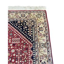 Persian design crimson ground rug, the field decorated with tree of life and floral motifs, enclosed by indigo spandrels with stylised flower head decoration, repeating scrolling border 