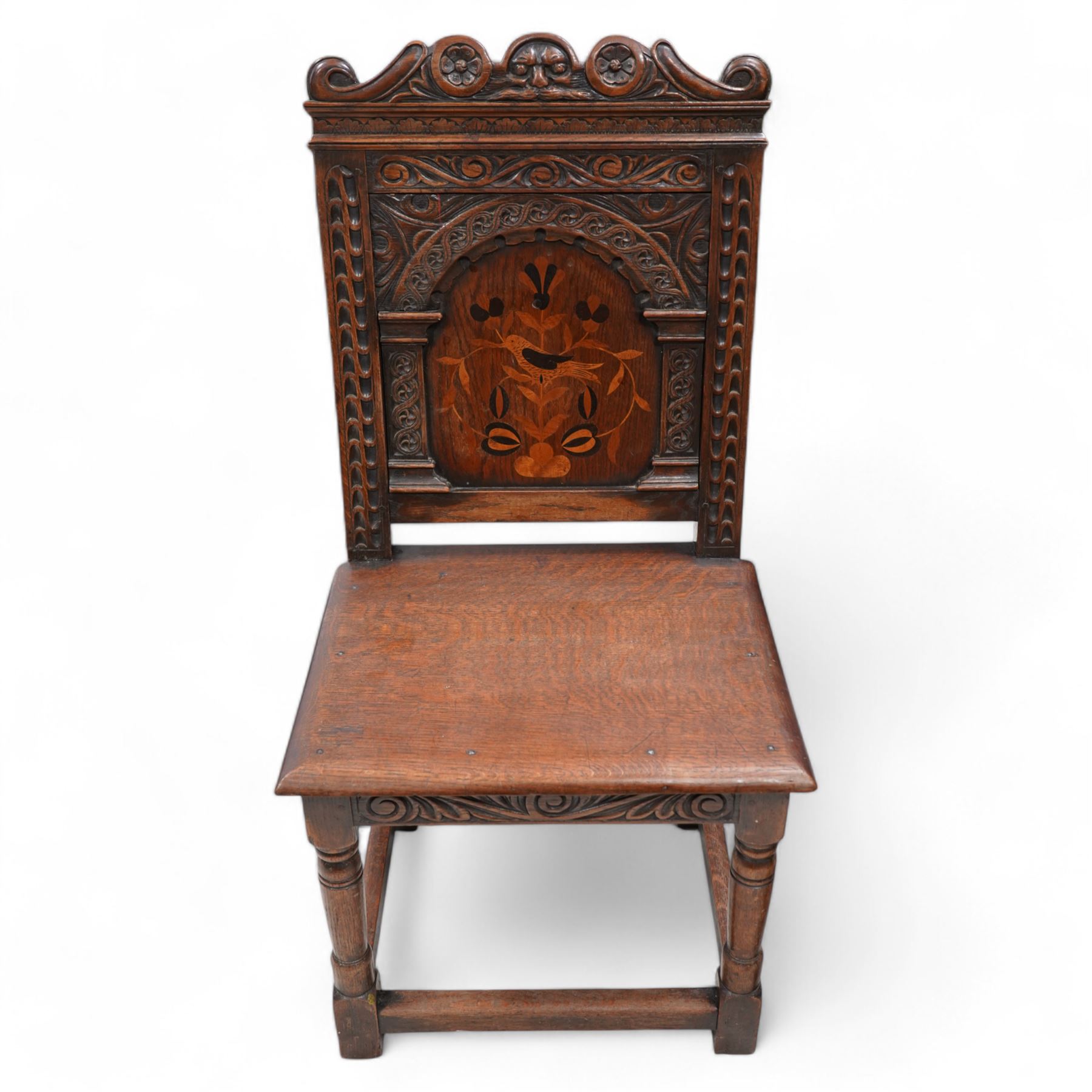 Pair of 19th century Dutch style marquetry oak hall chairs, cresting rail carved with a central green man mask with flanking scrolls, the panelled back inlaid with a bird motif within a guilloche carved arch, panelled seat over scrolling foliate carved apron, on ring turned supports united by box stretcher