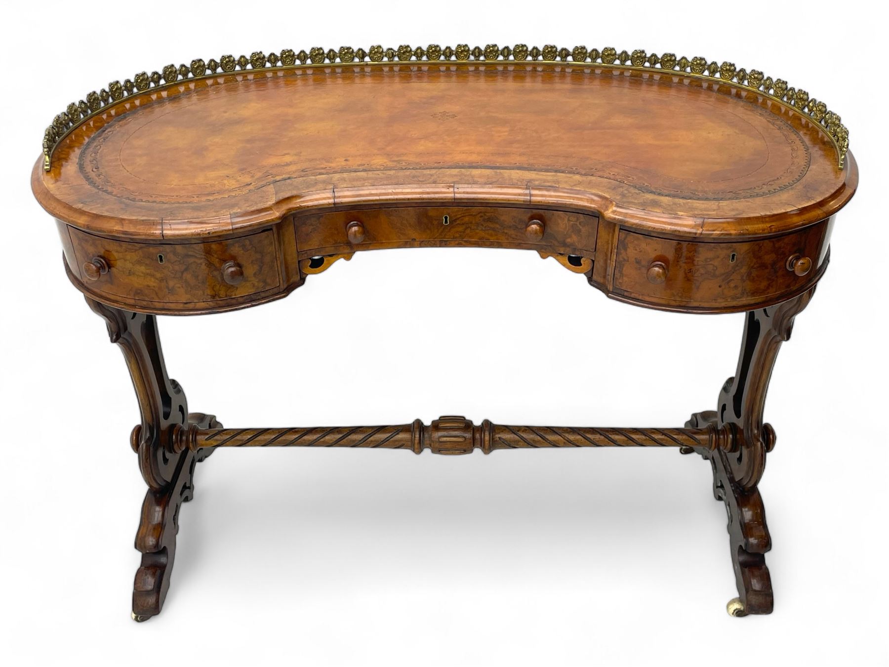 Victorian walnut kidney-shaped writing desk, moulded top with floral cast brass gallery and inset leather writing surface, fitted with three frieze drawers with turned handles, shaped and pierced end supports on raised platforms terminating to splayed feet, united by twist turned and lobe carved stretcher, brass and ceramic castors 