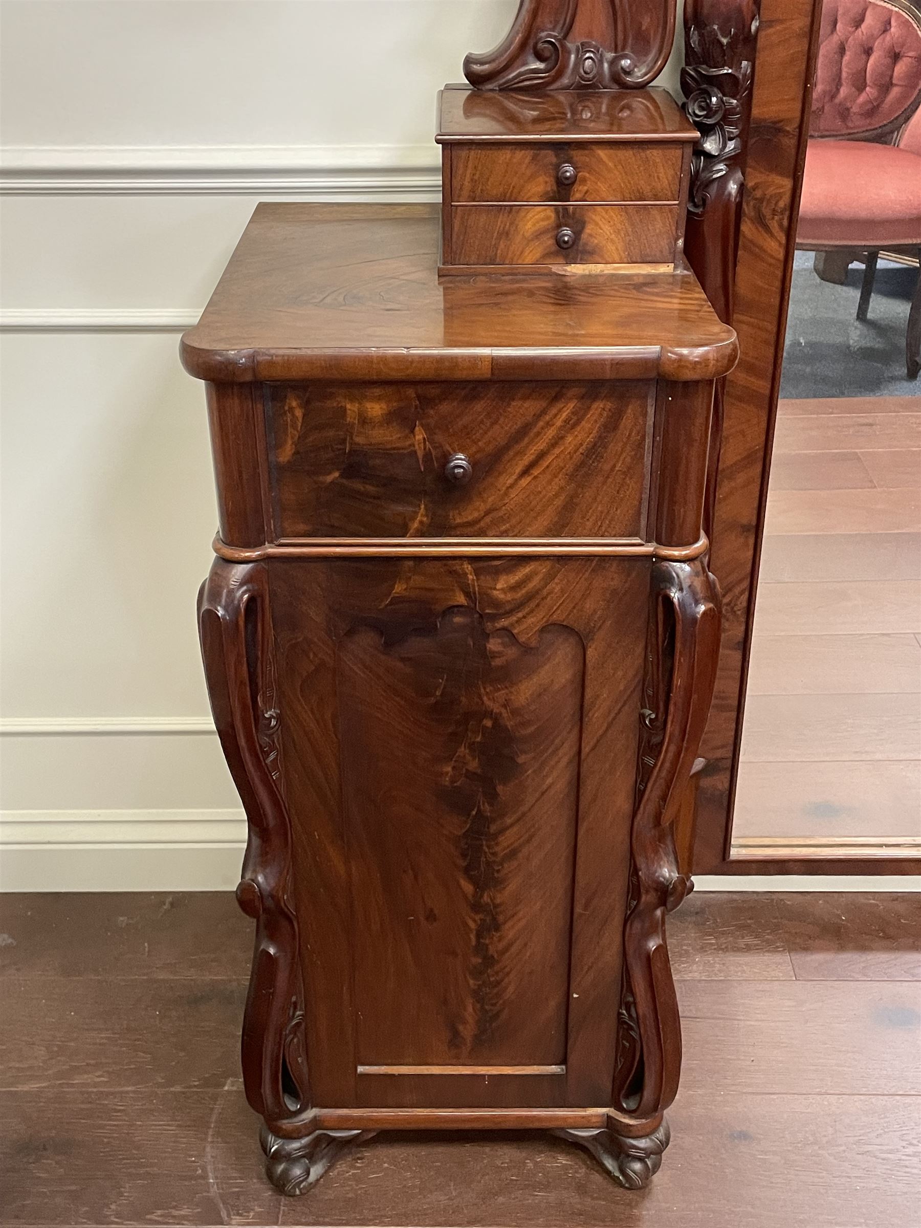 Tall Victorian figured mahogany twin pedestal dressing table, the tall mirror with flower head and scrolled leaf carved pediment, flanked by two turned and carved finials over faceted lancet arched lantern tops, plane mirror plate enclosed by shaped frame, pierced and undulating moulded uprights, on C-scroll and curled leaf carved supports fitted with cast brass hinged candle sconces, each pedestal fitted with two small trinket drawers over larger drawer and panelled cupboard, canted corners with matched upright mounts, the cupboard doors enclosing slides, on scroll carved feet 