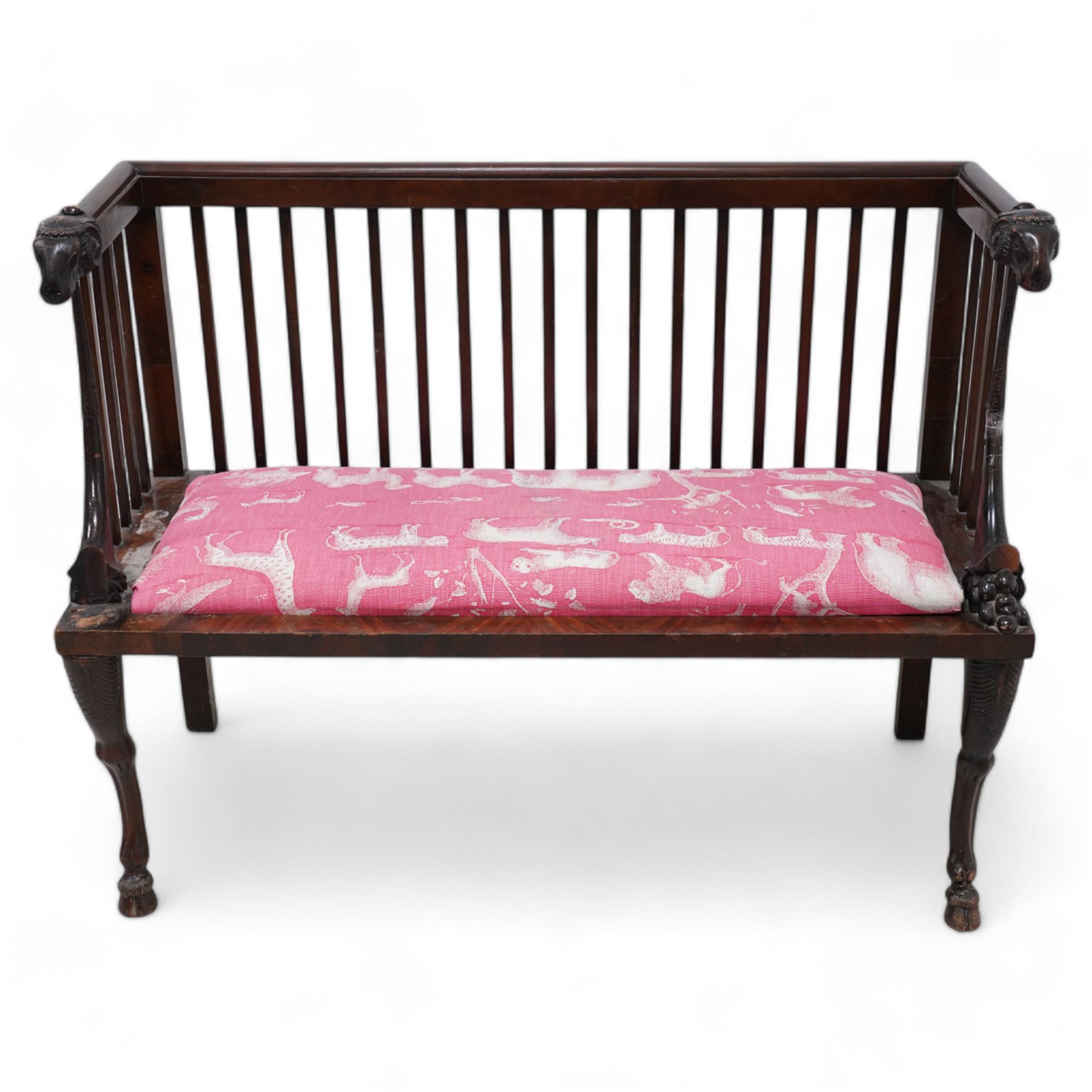 19th century mahogany two-seat bench, moulded cresting rail over slatted back with rams head carved terminal, the front arm supports in the form of fruit cornucopias, rectangular seat upholstered in pink fabric decorated with animals, anthemion carved supports carved as rams legs with hoof terminals 