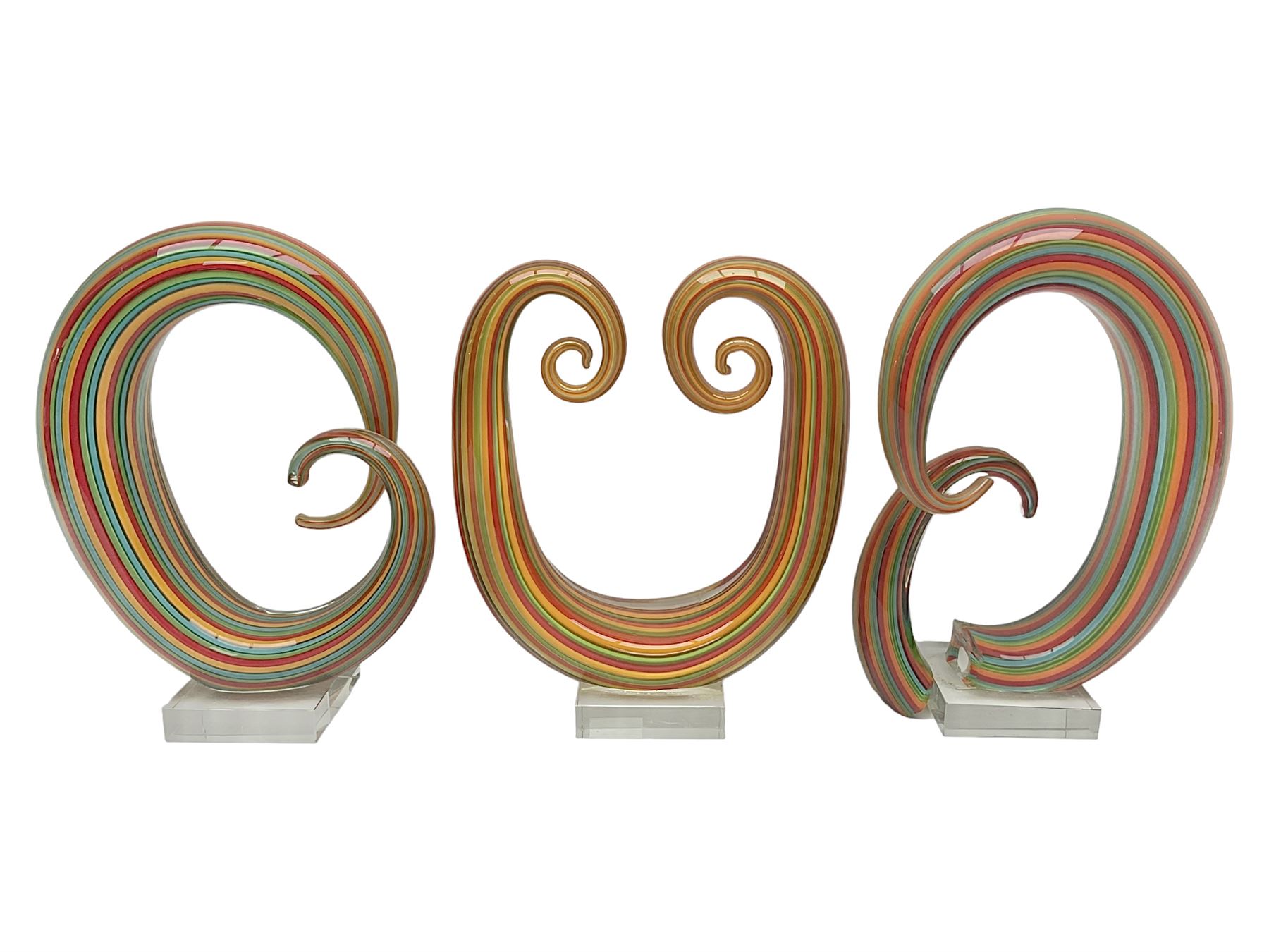 Three art glass sculpture, coiled form with multicolour stranded, upon clear glass plinth, unsigned, largest H27cm