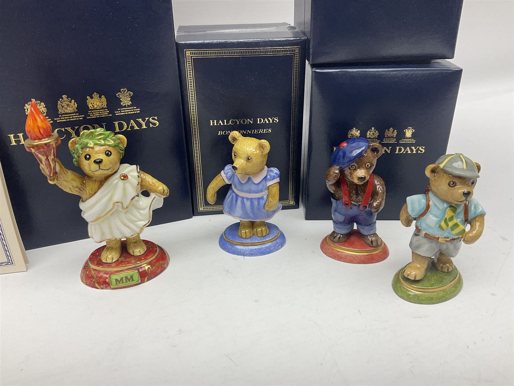 Eight Halcyon Days Teddy Bear of the Year figures, from 1993 to 2000, including one example modelled as a bear in Greek dress carrying a torch, one example modelled as a schoolboy and one example in a blue dress, all boxed 