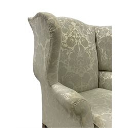 Georgian mahogany framed wingback armchair, upholstered in floral pattern silk damask fabric, wide seat enclosed by rolled arms, on chamfered square supports united by plain stretchers 