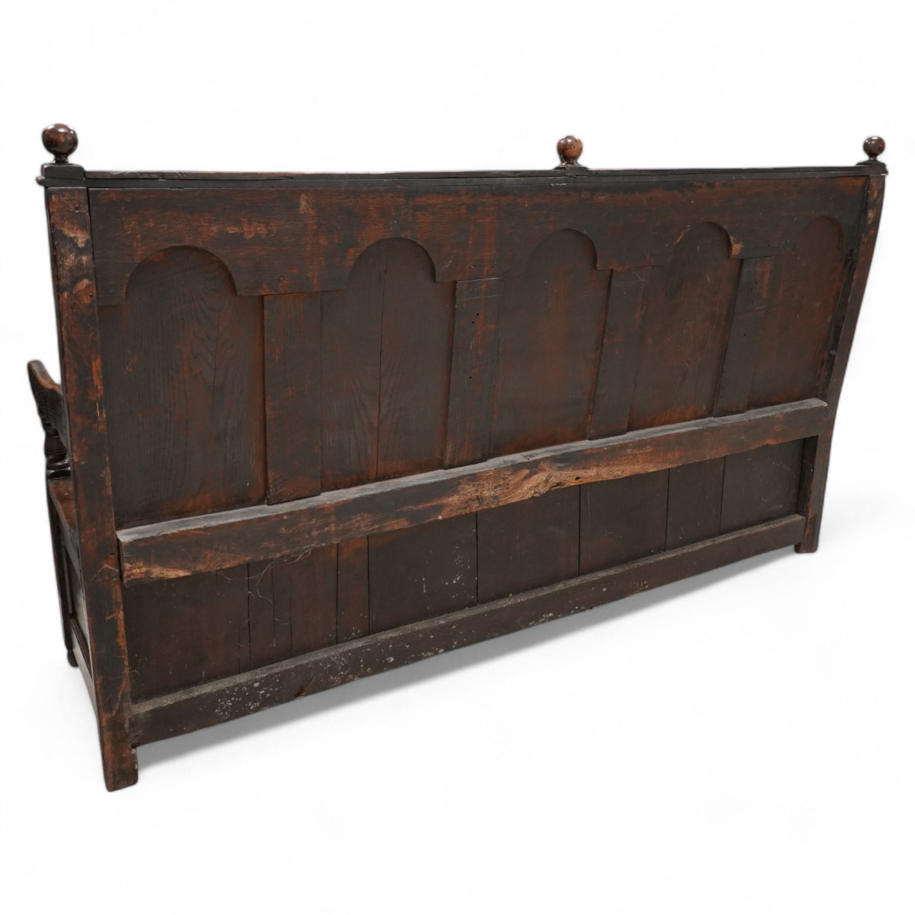 18th century oak settle or bench, moulded cresting rail with globular finials over five panel back, each stepped arch panel carved with stylised leaf decoration, hinged box seat over S-scroll foliate frieze and two panels carved with scrolling pattern, panelled sides, on stile supports terminating to turned feet 