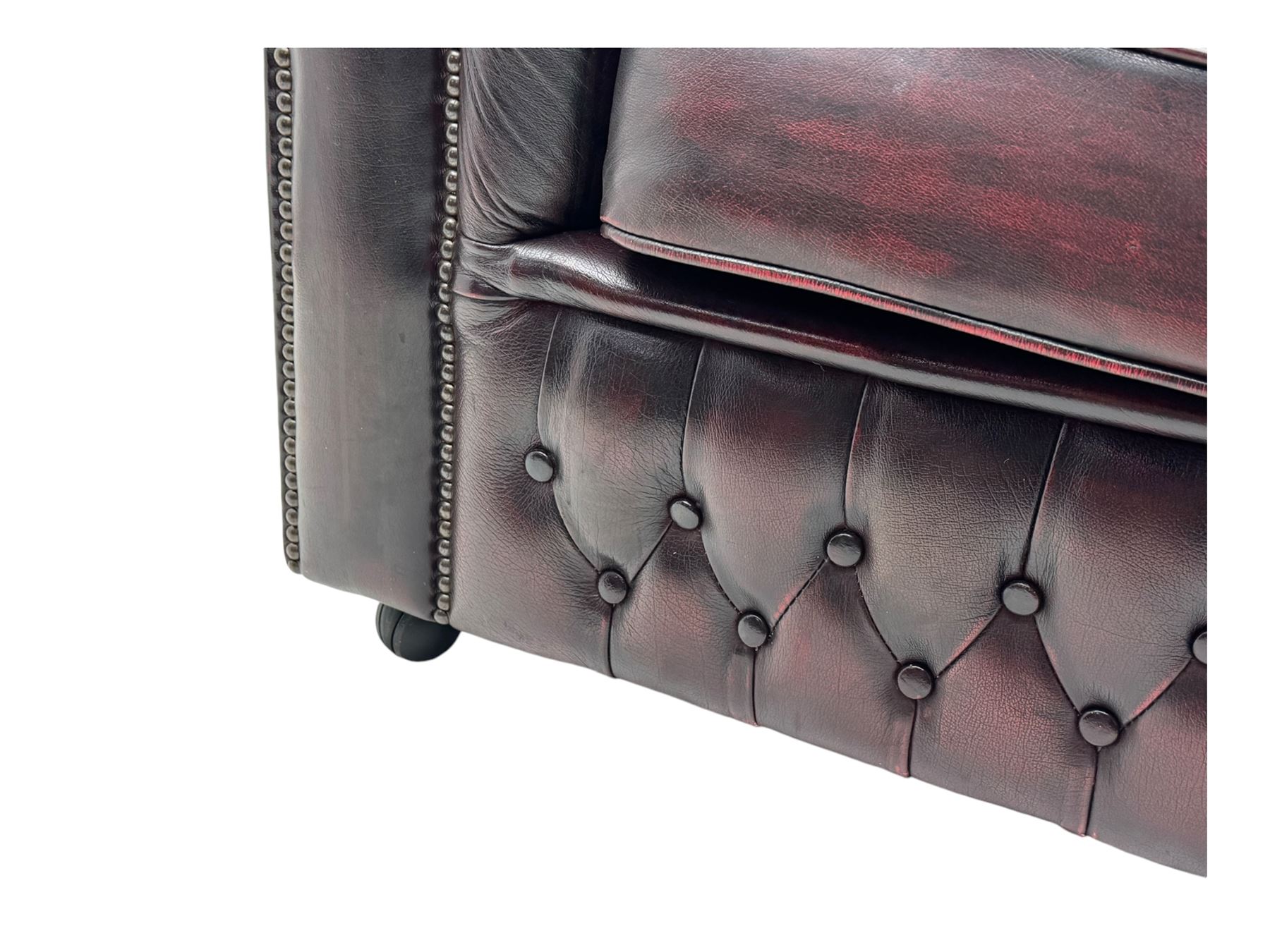 Chesterfield three-seat sofa, traditional shaped upholstered in deeply buttoned dark red leather; together with similar footstool 