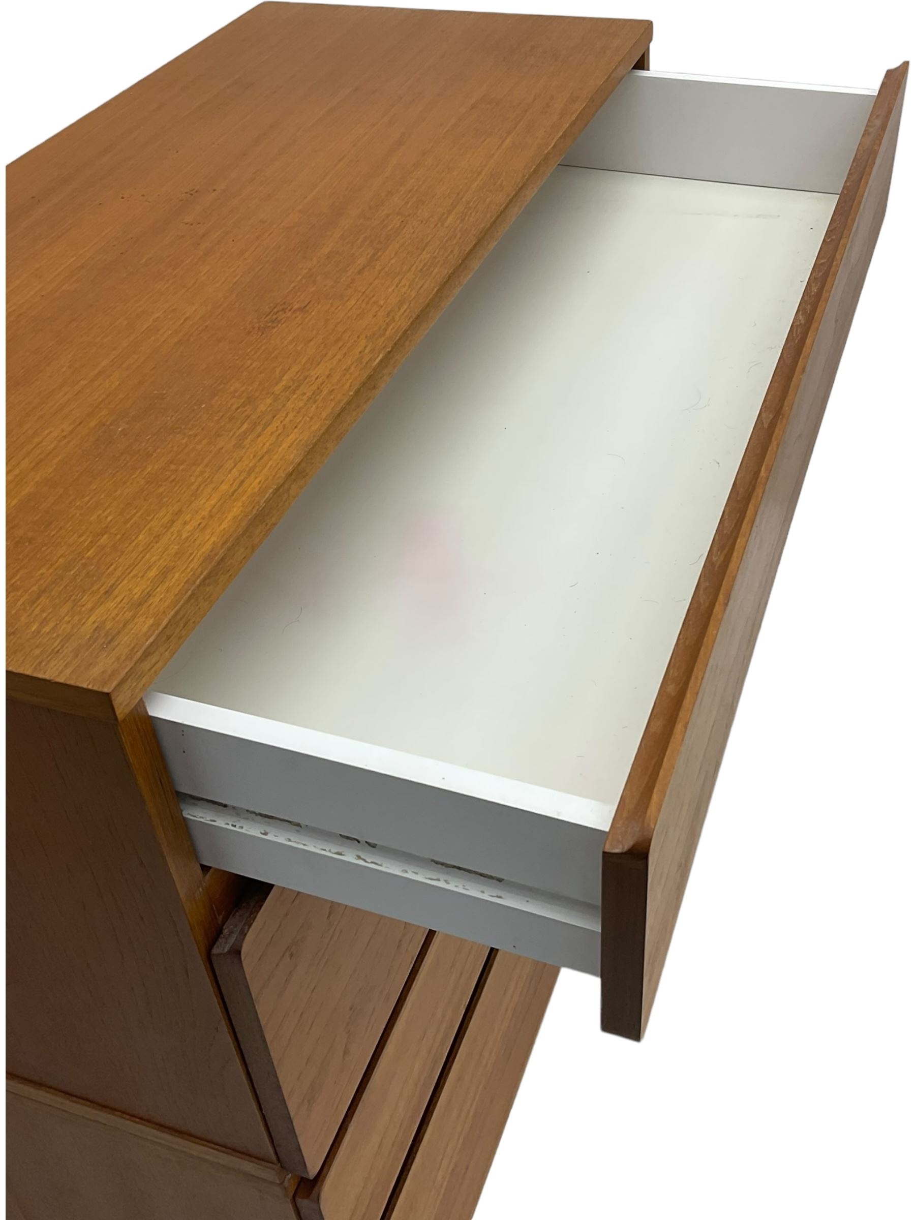 Mid-20th century teak four-drawer chest, featuring a minimalist design with two shallow and two deep flush drawer fronts, each with recessed handles along the top edge, the drawers open to reveal white laminate interiors, supported by castors