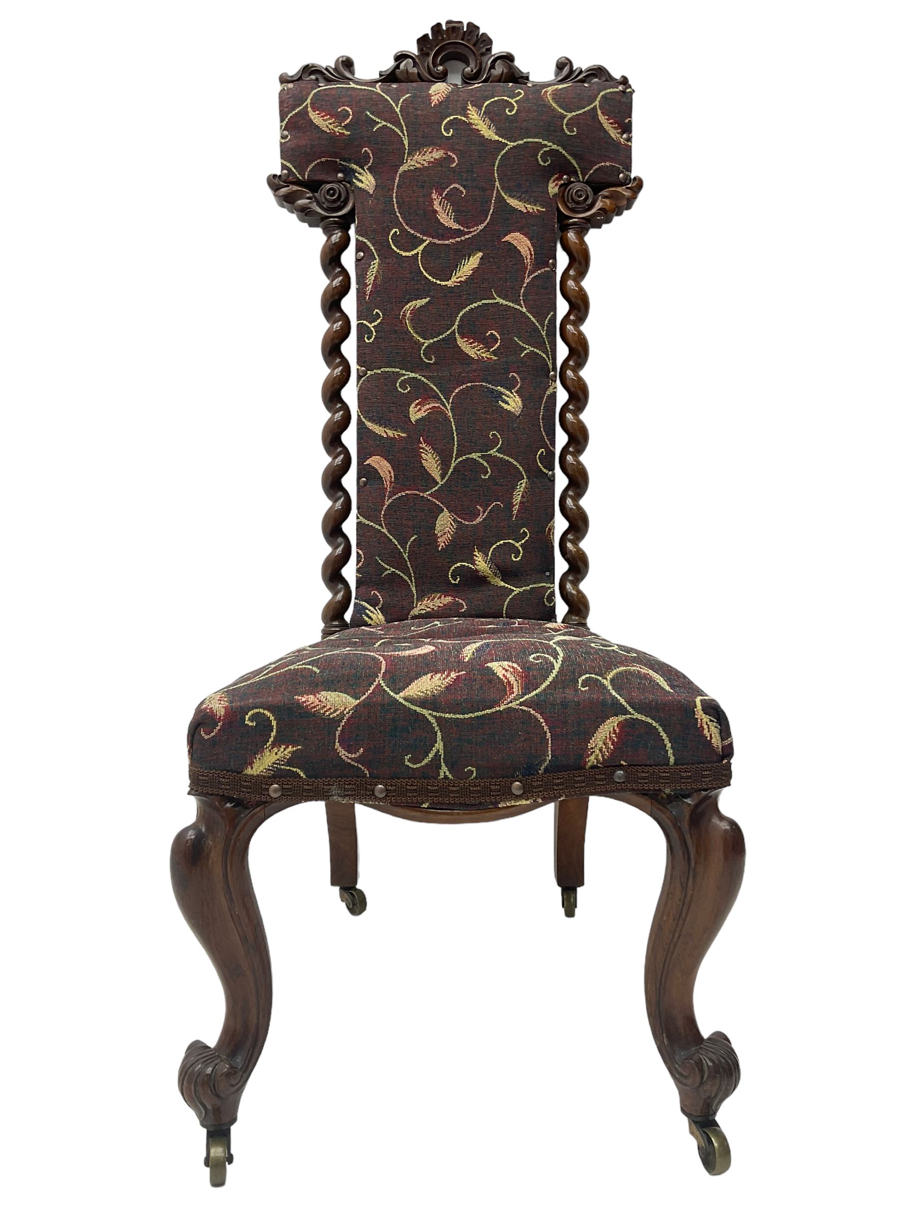 Victorian walnut prie-dieu chair, cresting rail carved with cartouche and extending scrolling foliage, back flanked by spiral turned column uprights, upholstered in foliate patterned fabric, raised on cabriole supports with scroll feet and castors