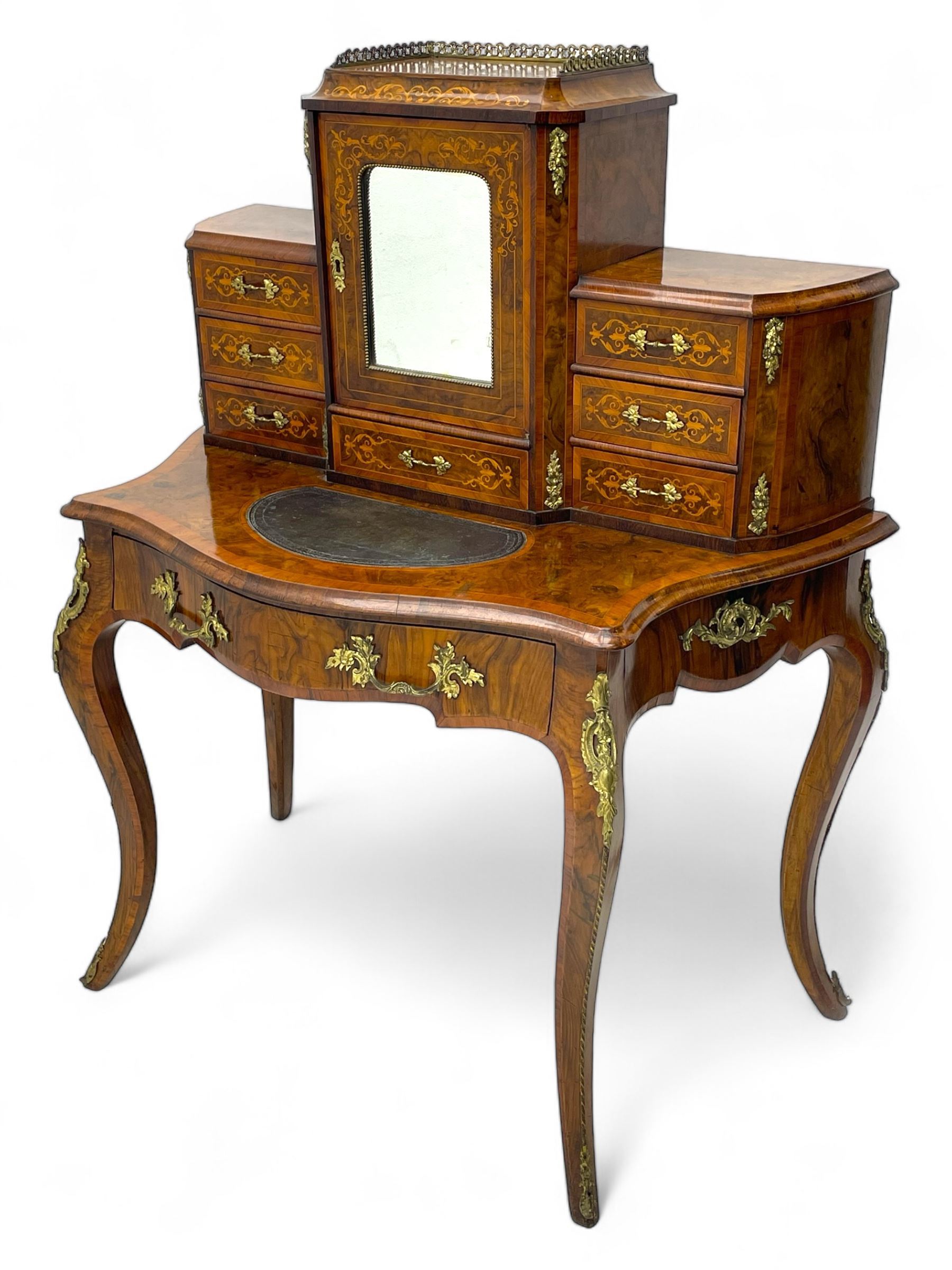 19th century French figured walnut Bonheur de Jour or writing desk, the upper section with brass gallery over mirror glazed cupboard and a combination of drawers, shaped and moulded top with leather inset and satinwood band, fitted with single drawer, on cabriole supports, inlaid throughout with scrolling foliate decoration in boxwood, ornate cast brass mounts 