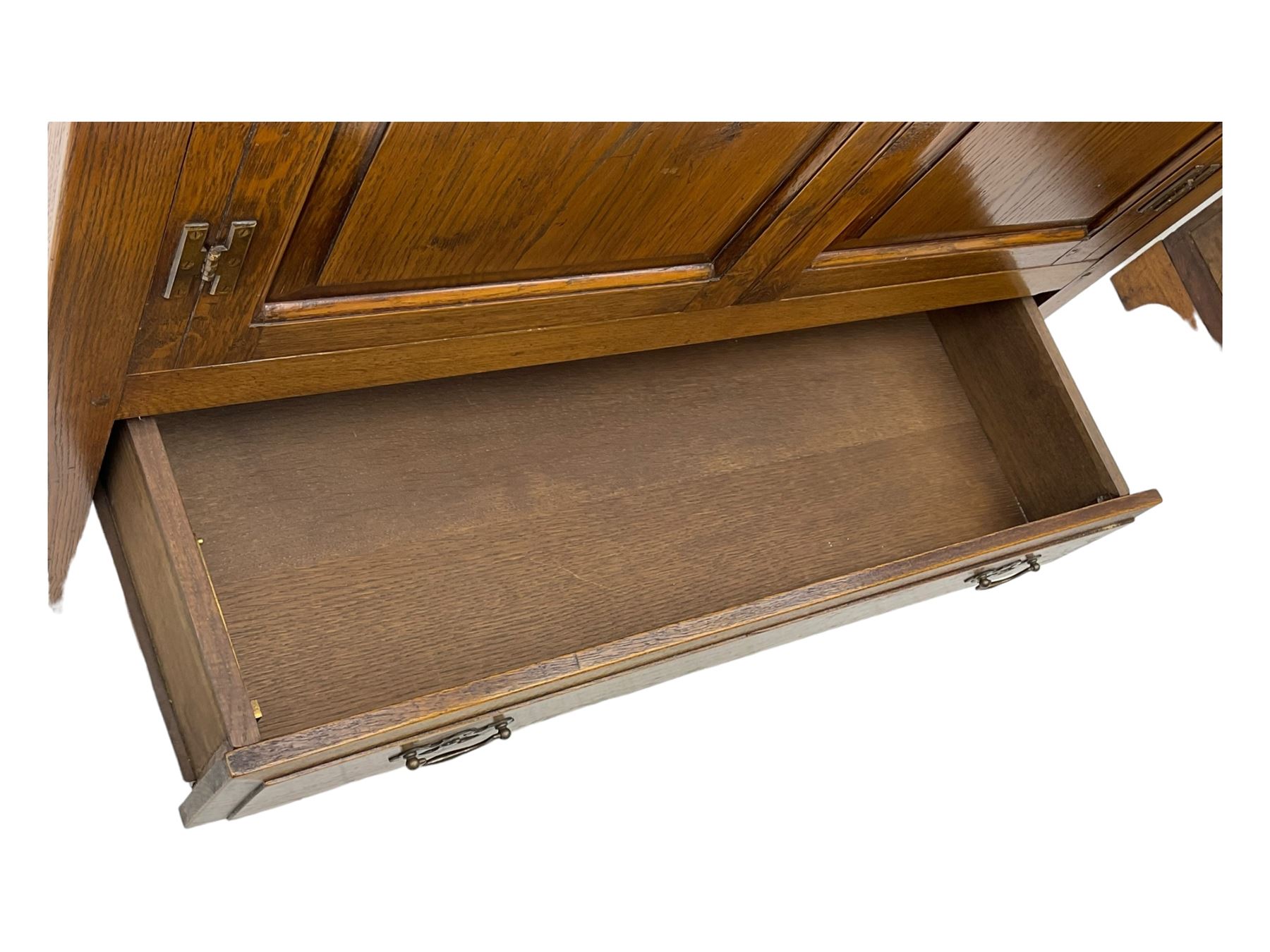 Oak drinks or media cabinet, projecting moulded cornice over two Gothic arch panelled doors on sliding tracks enclosing open storage, two drawers with brass drop handles, on bracket supports