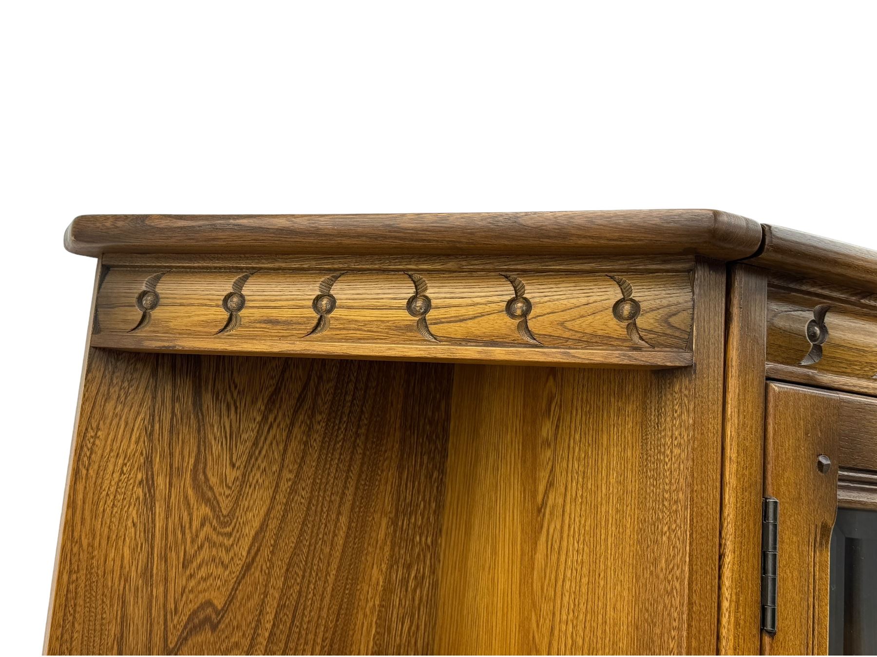 Ercol - elm three sectional wall cabinet, the central unit with raised display cabinet enclosed by bevel glazed doors, fitted with two drawers over two panelled cupboards, flanked by two corner units fitted with shelves and panelled cupboards 