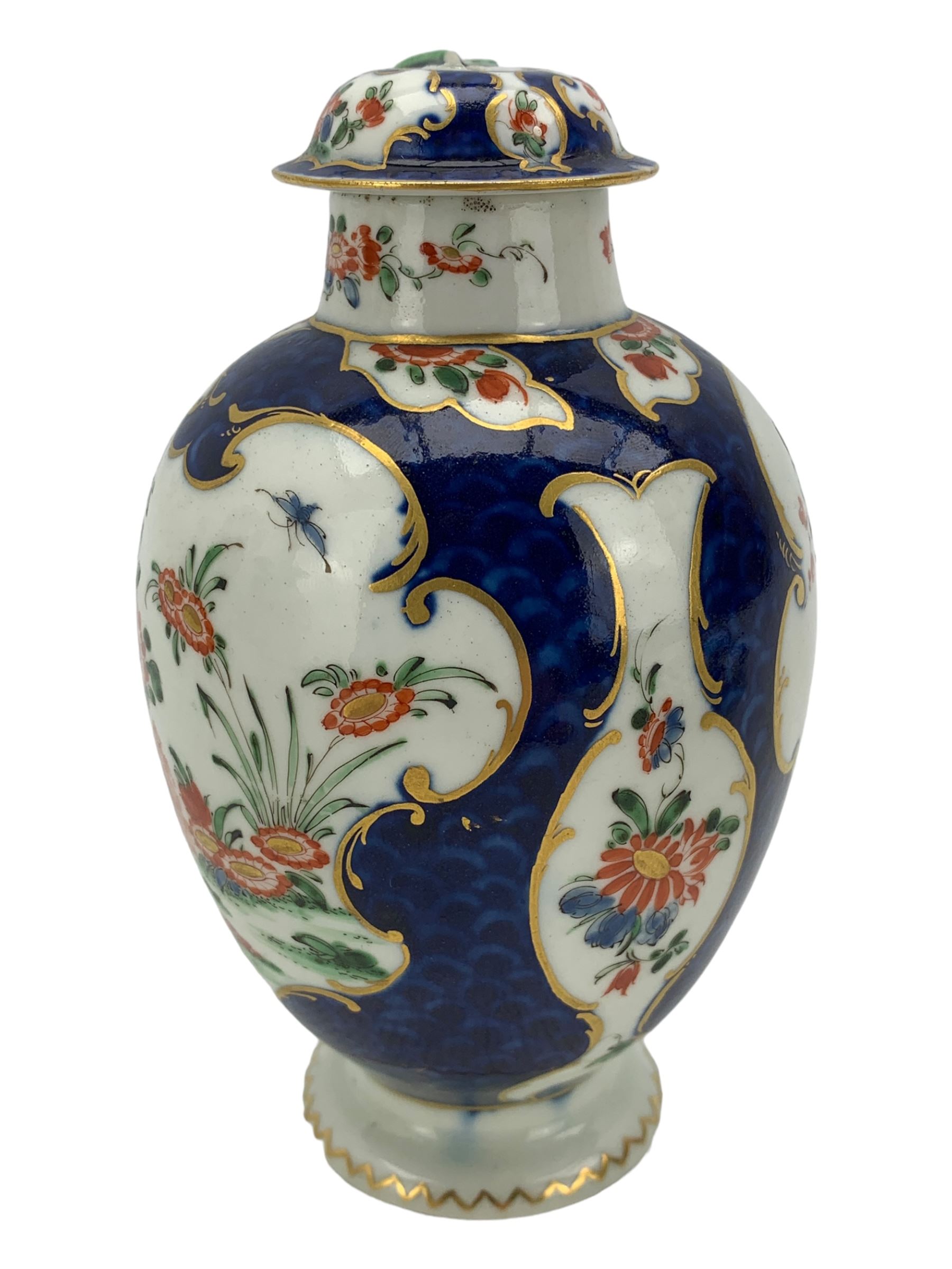 18th century Worcester tea caddy, of oval form and painted in the Kakiemon palette with reserves of flowers against a blue scale ground, H14cm together with a similar Worcester circular dish, painted with floral sprays, within a scalloped edge, blue crescent mark beneath, D19cm (2)