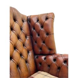 Georgian design hardwood-framed wingback armchair, shaped cresting rail and deep wingback over rolled arms, upholstered in brown buttoned leather with studwork bands, the seat cushion upholstered in checkered fabric, on square supports united by stretchers (W86cm, H118cm, D86cm); together with matching rectangular footstool (63cm x 43cm, H37cm) 